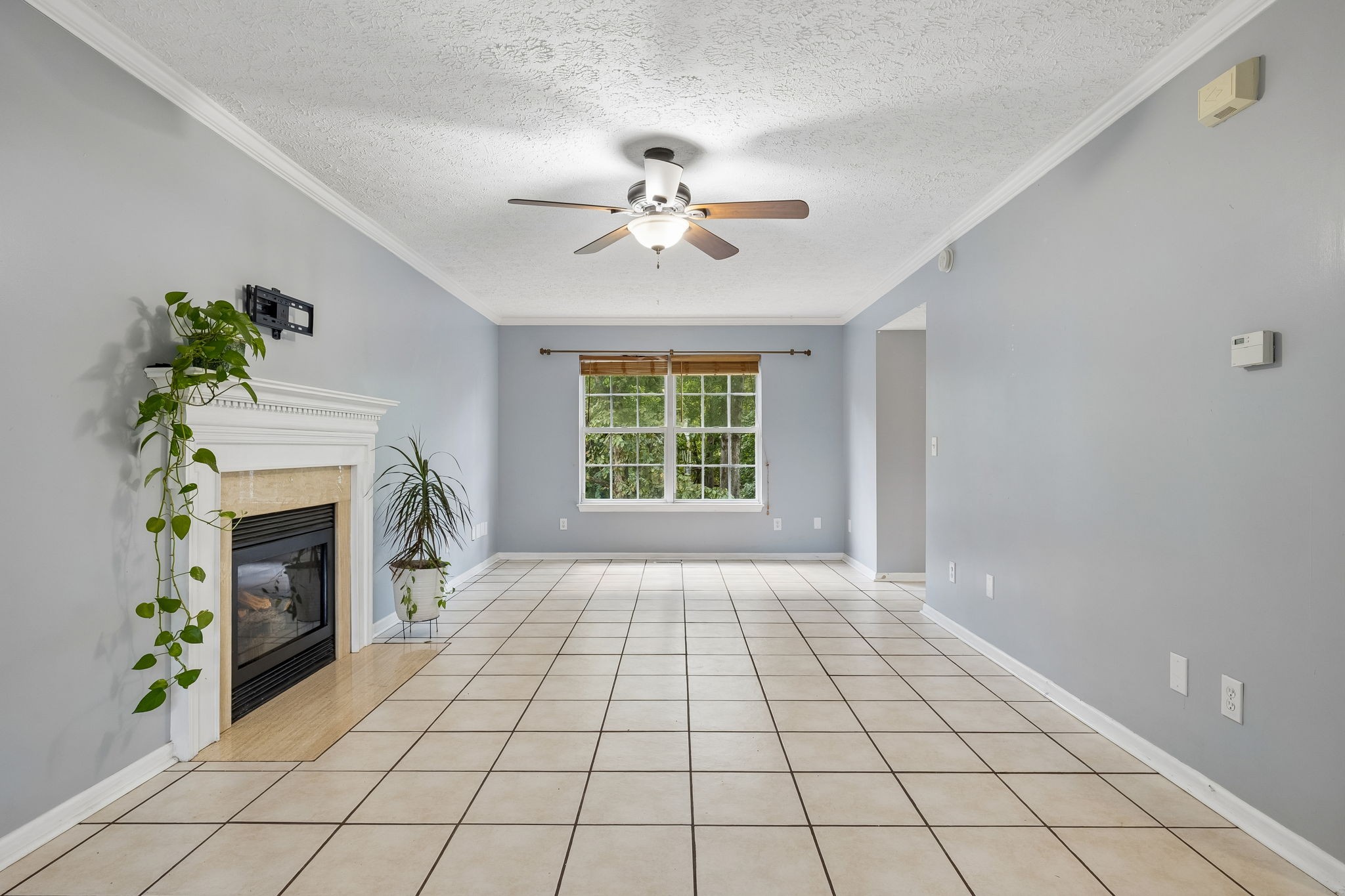 Unfurnished living room with tiled floors, a gas fireplace, ceiling fan, and window overlooking greenery.