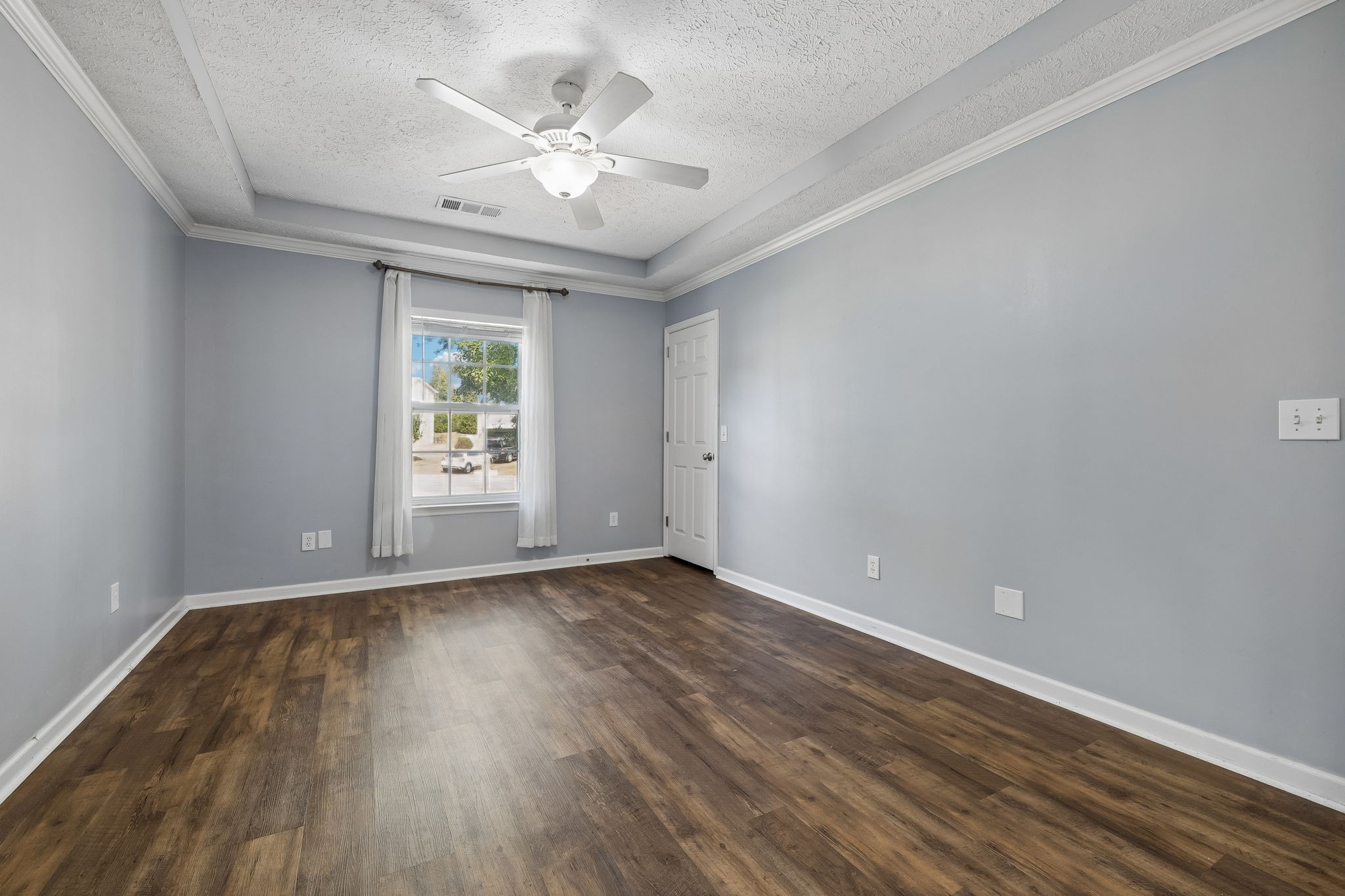 Empty room with dark wood-look flooring, gray walls, a curtained window, and ceiling fan.