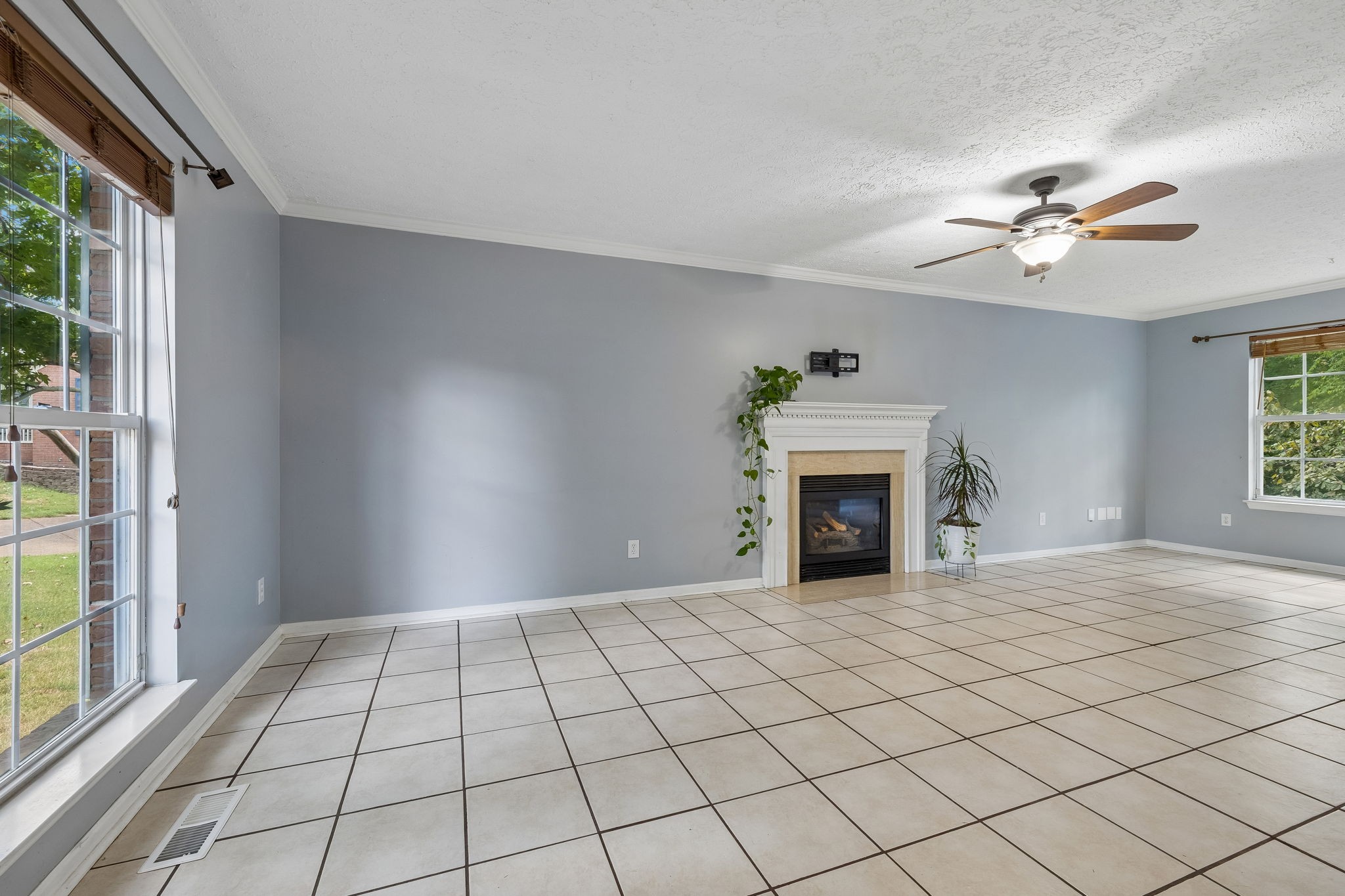 Living room with a tiled floor, white fireplace, ceiling fan, and large windows.