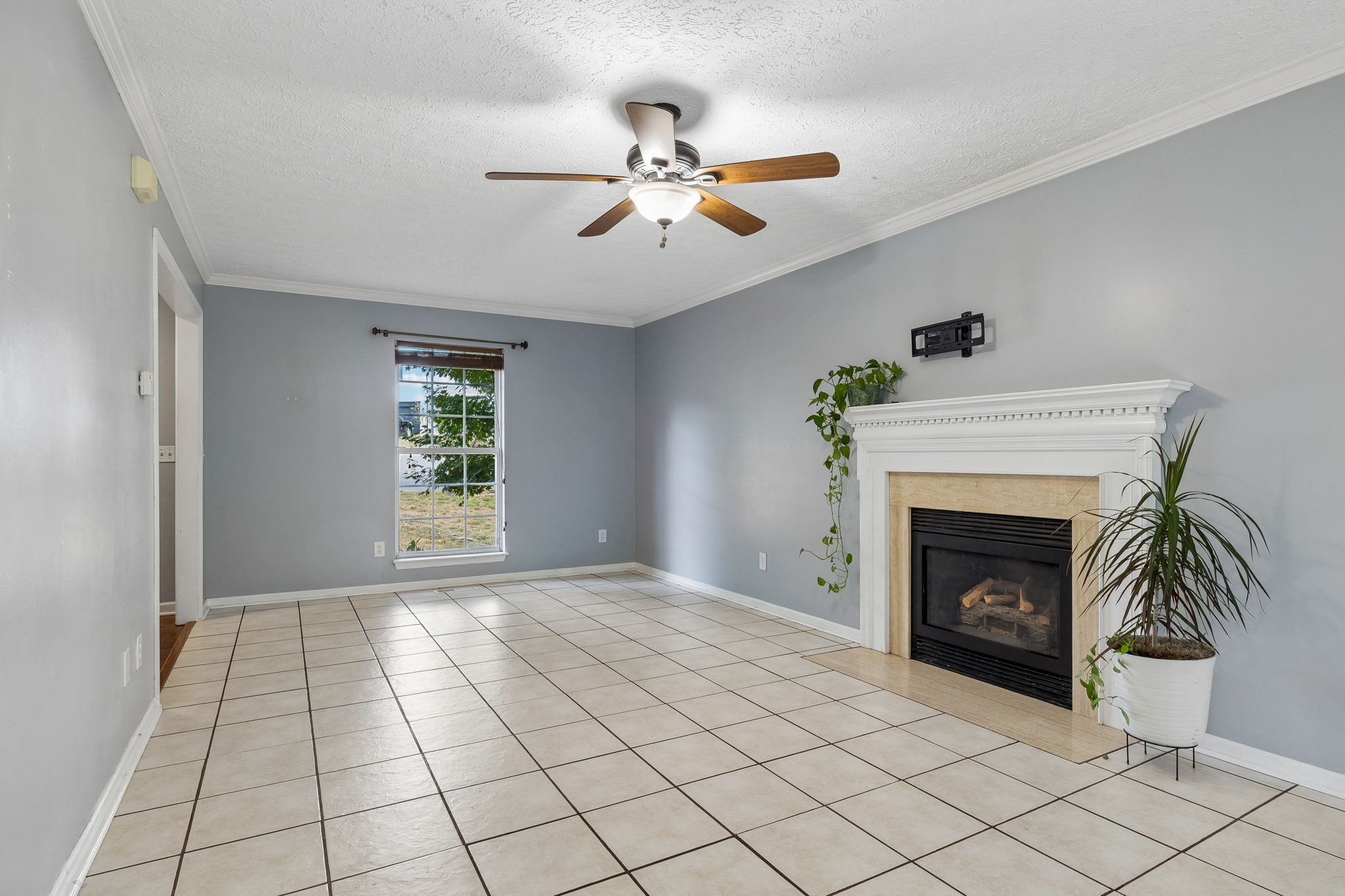 Living room with tiled floor, ceiling fan, and white fireplace with a gas insert.