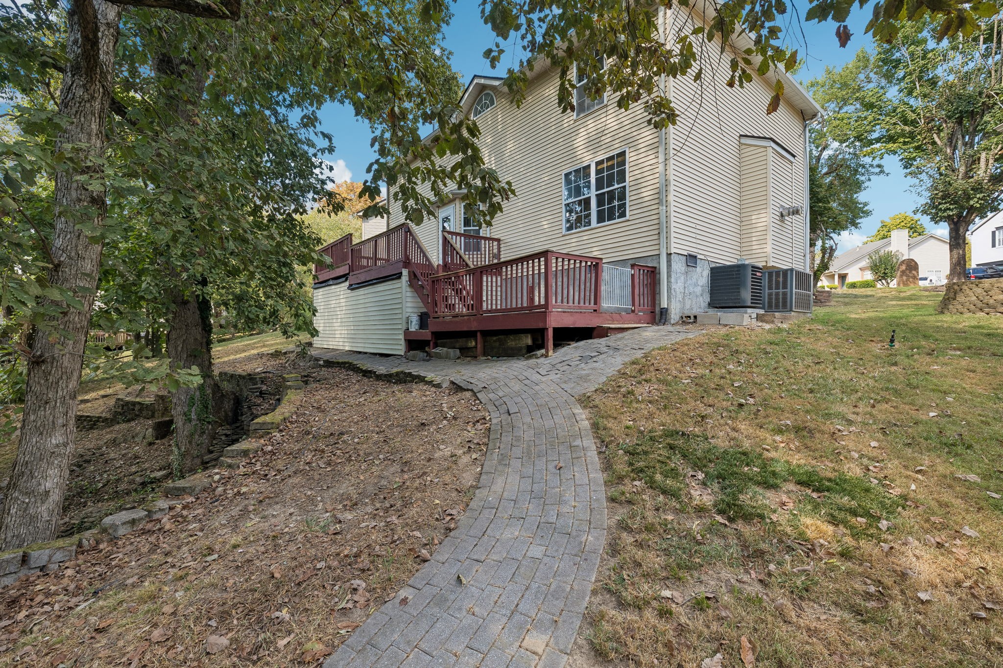 Rear of a two-story home with raised decks and a curved paver walkway through a wooded yard.