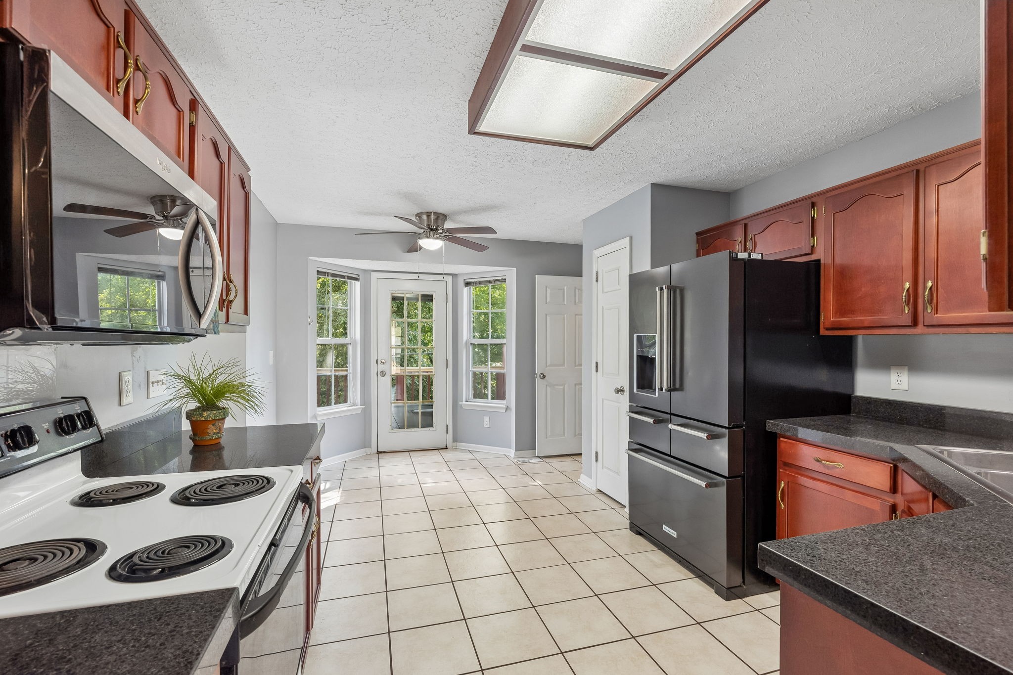 Kitchen with reddish wood cabinets, dark countertops, stainless refrigerator, and a glass-paneled door.