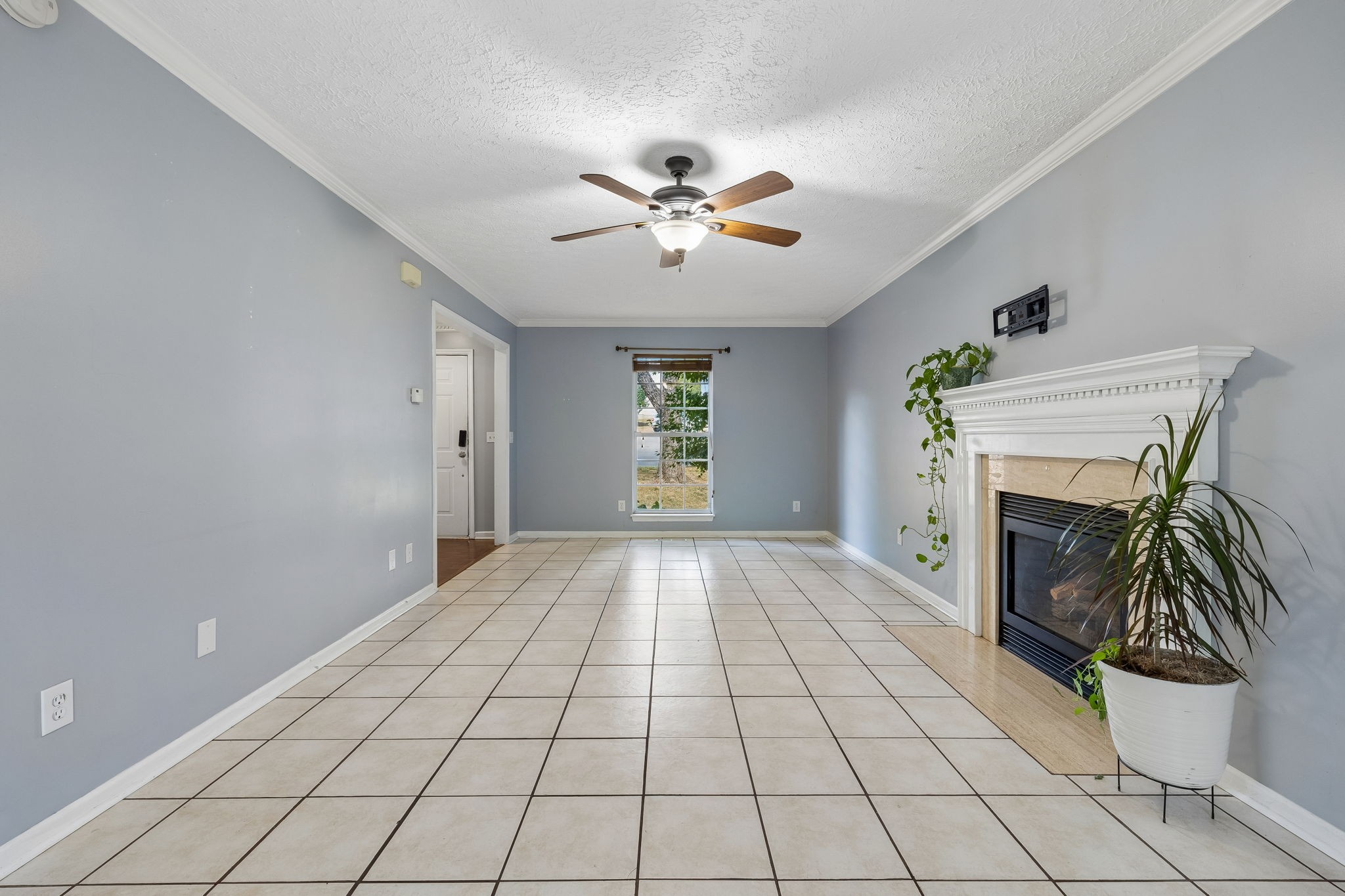 Empty tiled living room with a white fireplace, ceiling fan, and narrow window.