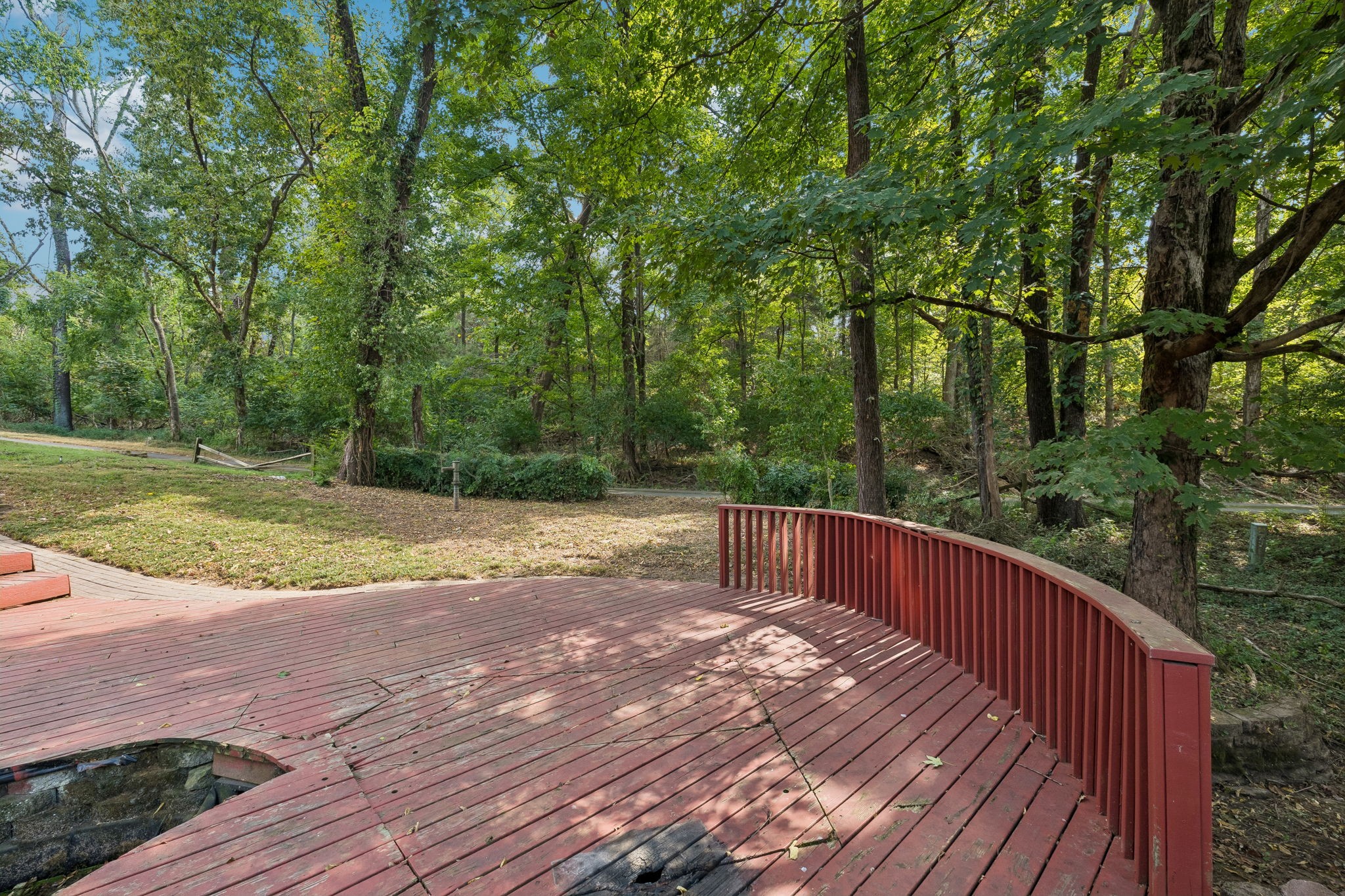 Red wooden deck with curved railing overlooking a leafy backyard and mature trees.