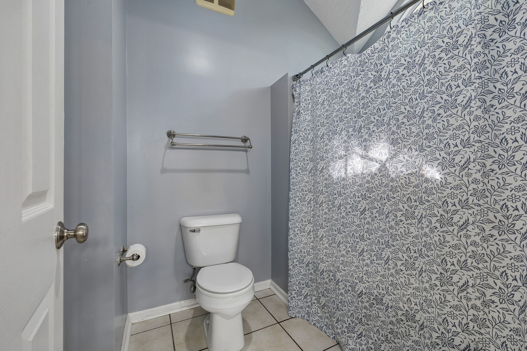 Bathroom with a white toilet and a floral-patterned shower curtain against gray walls.