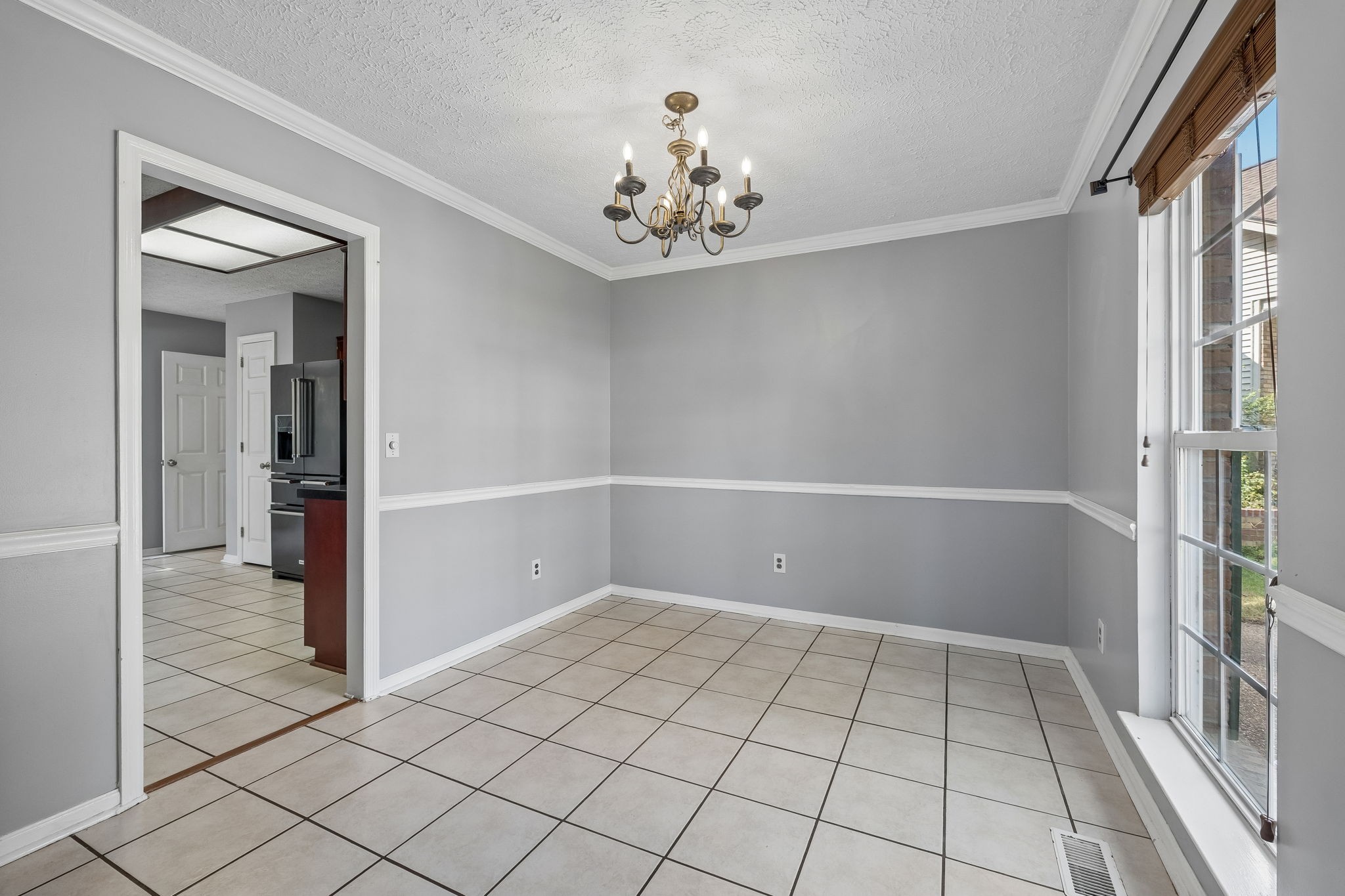 Empty dining room with tiled floors, a chandelier, and large windows with wooden blinds.