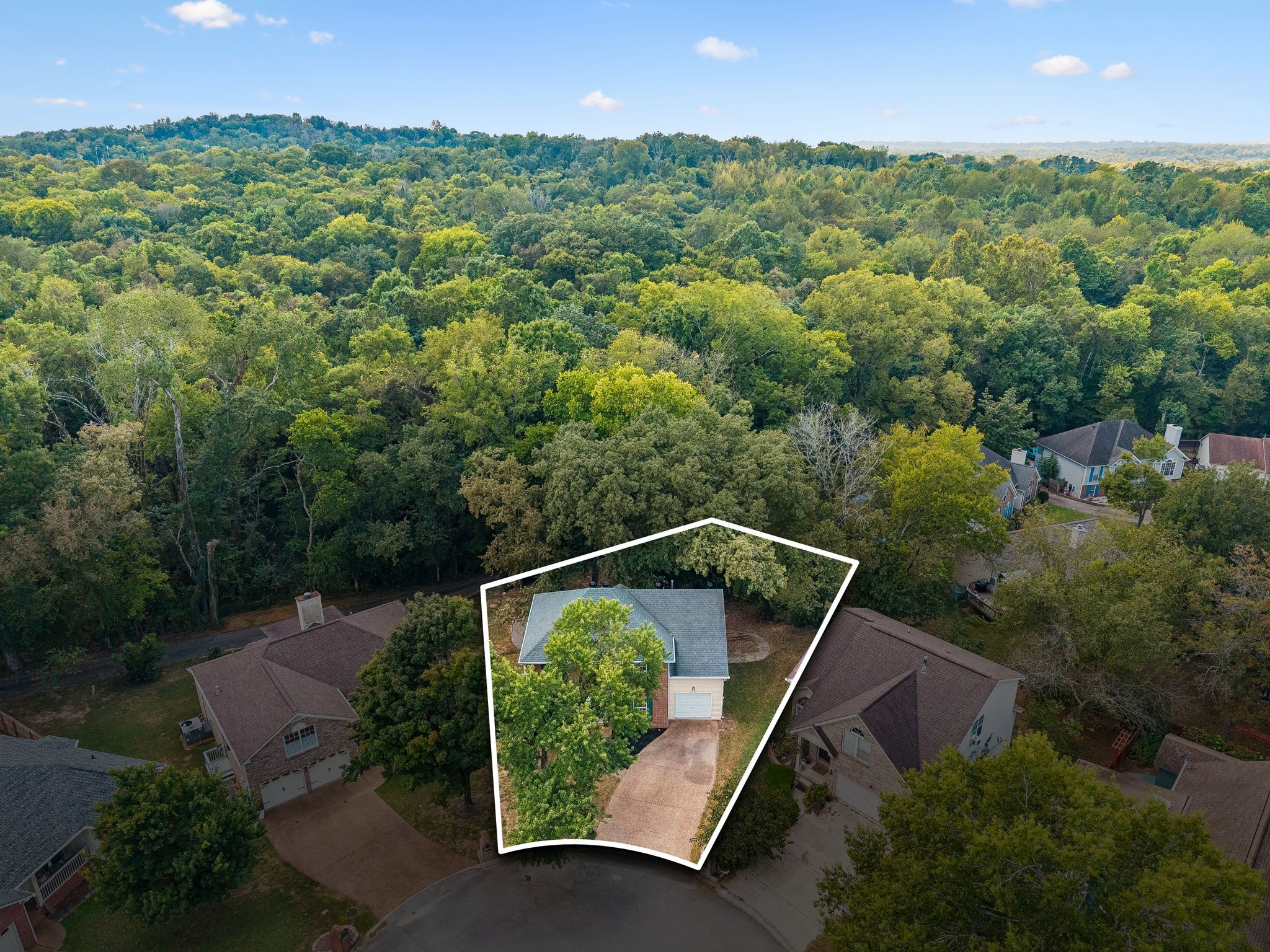Aerial view highlighting a home and driveway on a wooded lot among neighboring houses.