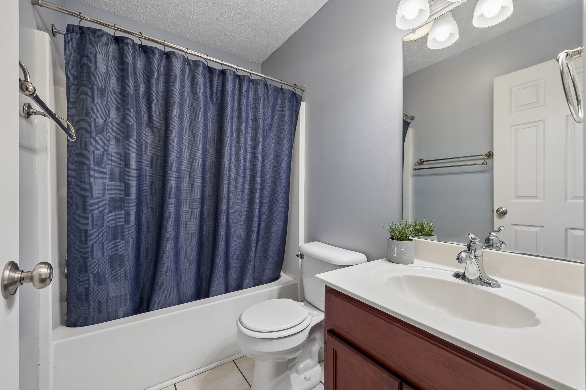 Bathroom with navy shower curtain, white tub and sink, and reddish wood vanity.