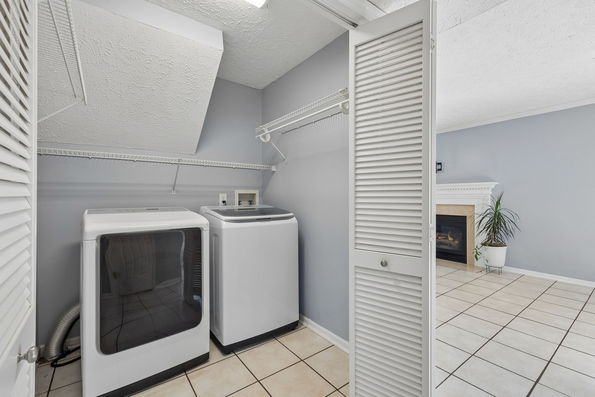 Laundry room with a front-loading dryer, top-loading washer, and wire shelving.