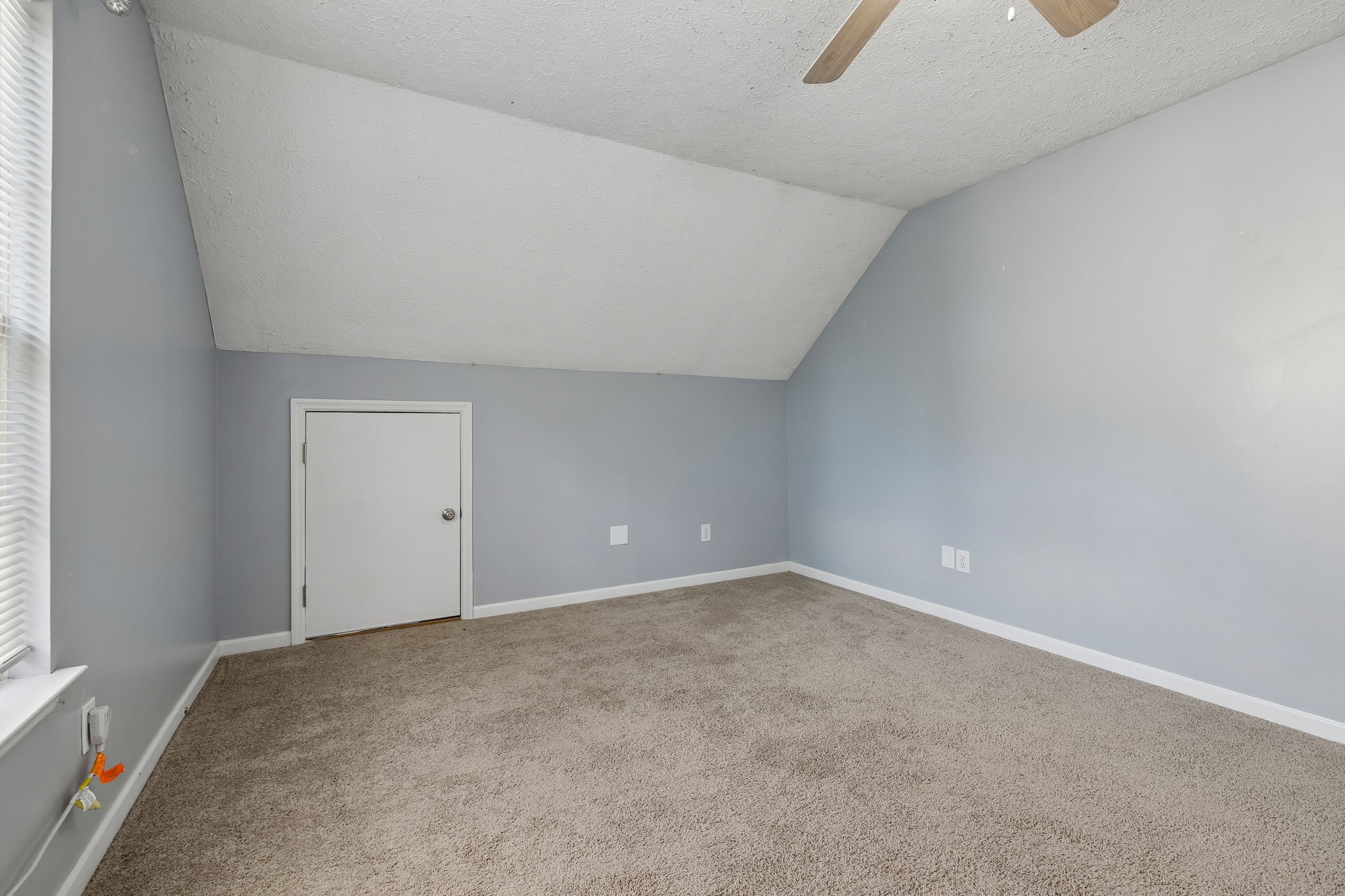 Empty carpeted bedroom with gray walls, a ceiling fan, and a window with white blinds.
