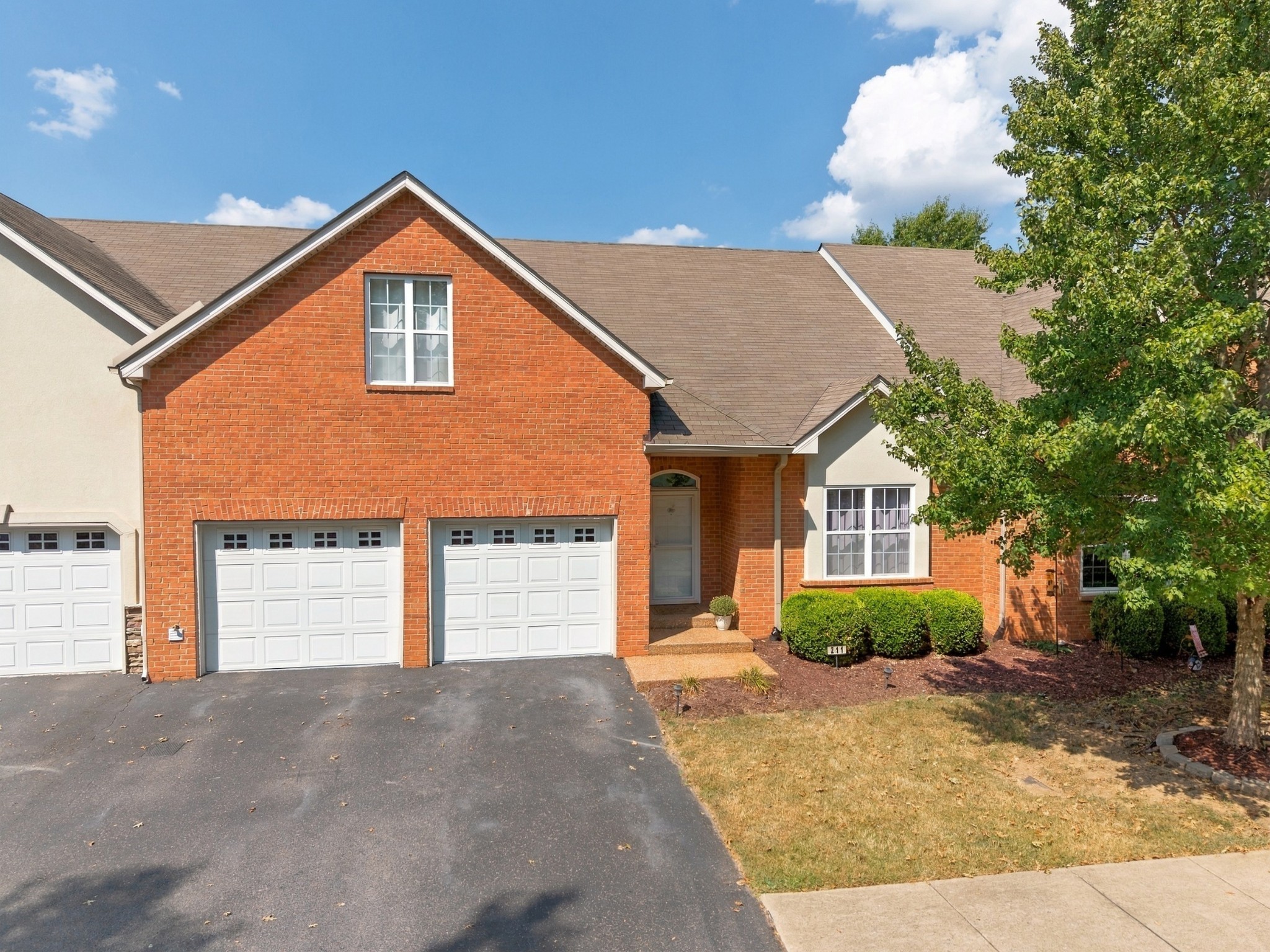 Red brick home with two white garage doors, a broad driveway, and landscaped front yard.