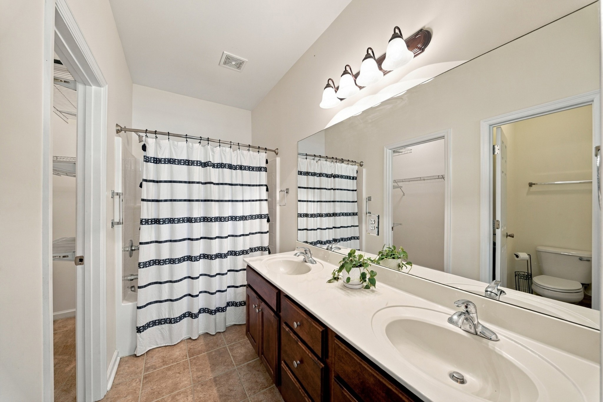 Bathroom with double sinks, dark wood vanity, striped shower curtain, and open doorway to the toilet area.