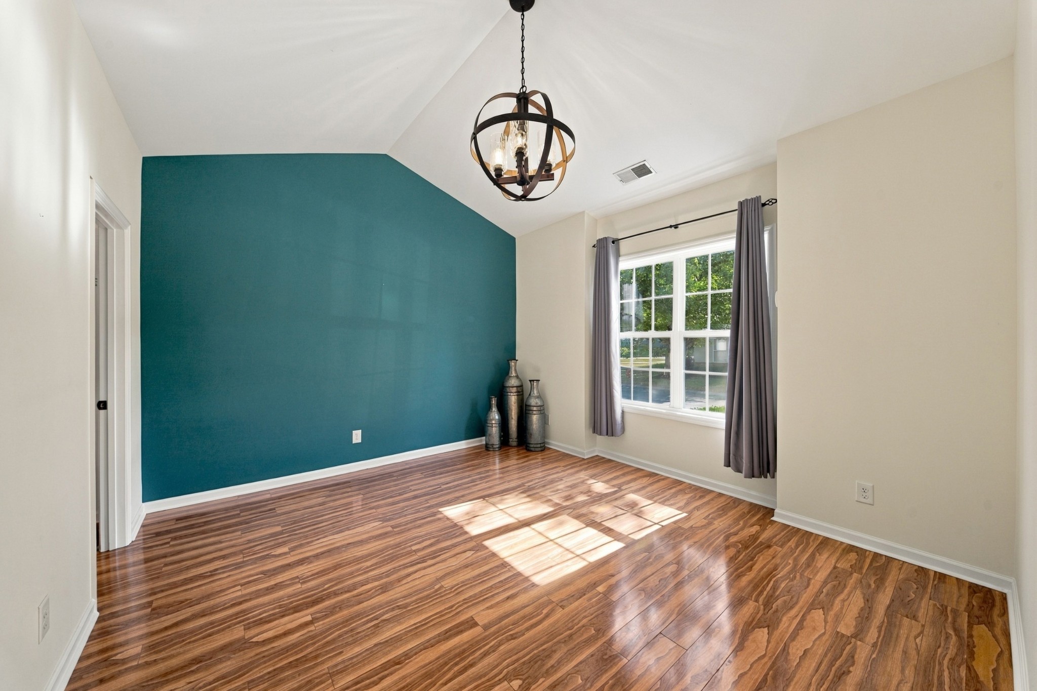Dining room with a teal accent wall, wood-look floors, and a dark metal chandelier.
