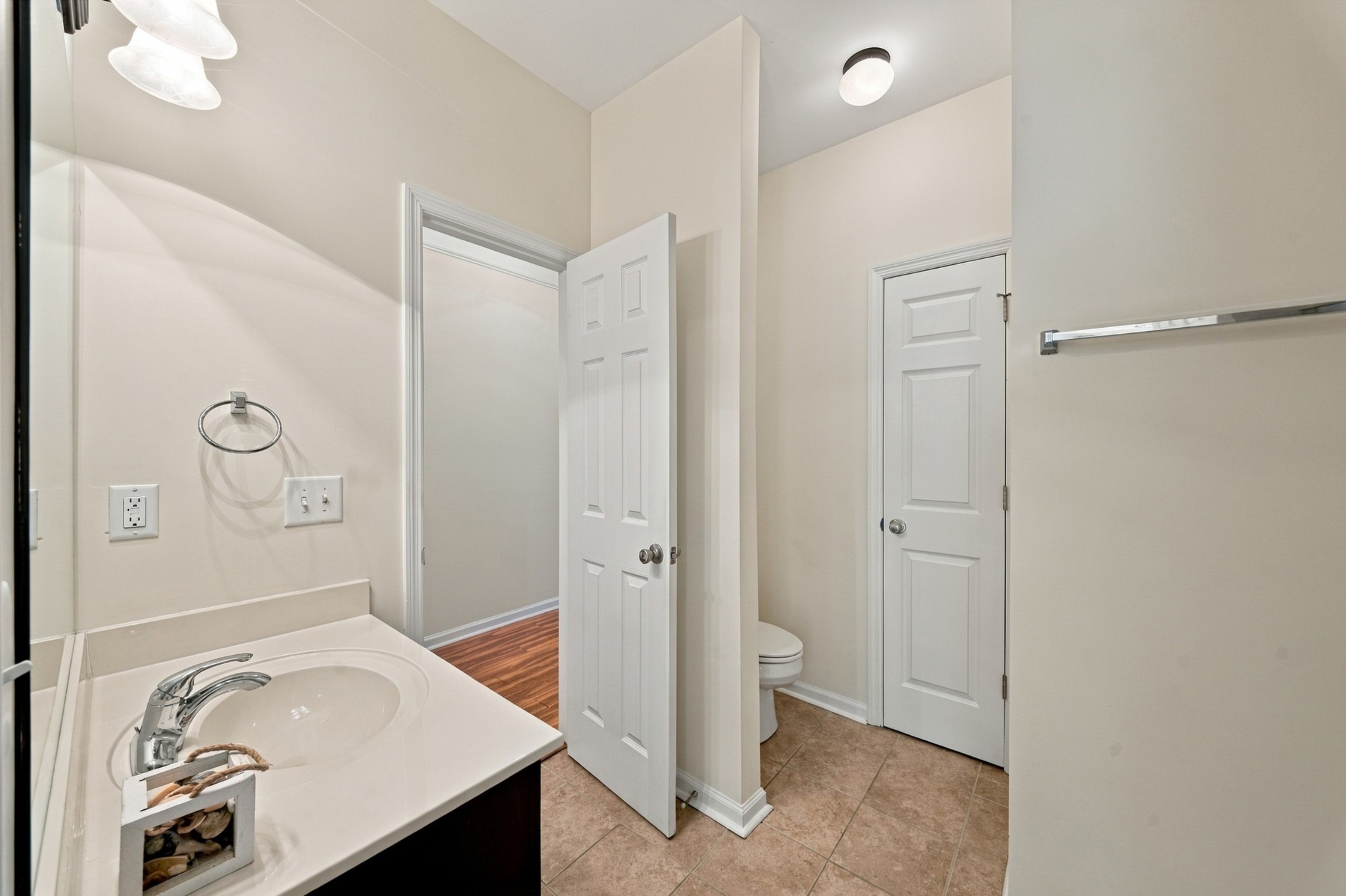 Bathroom with a white sink vanity, tiled floor, and toilet partly visible behind an open door.