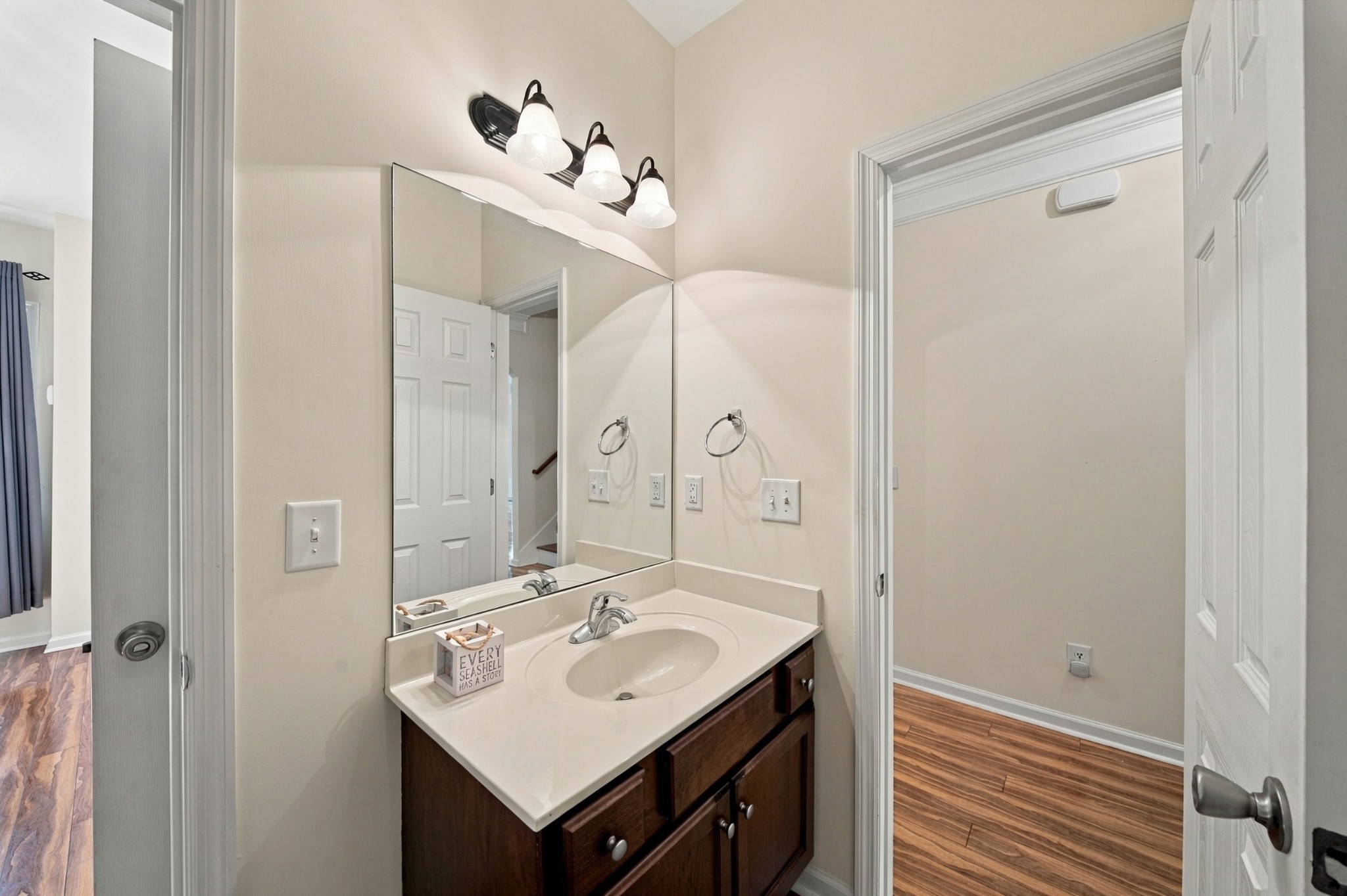 Bathroom vanity with an oval sink, dark wood cabinets, large mirror, and three-light fixture.