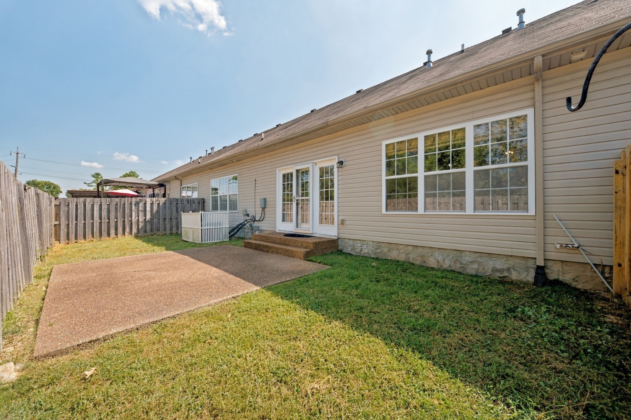 Home’s rear exterior with a concrete patio, large windows, and a fenced grassy backyard.