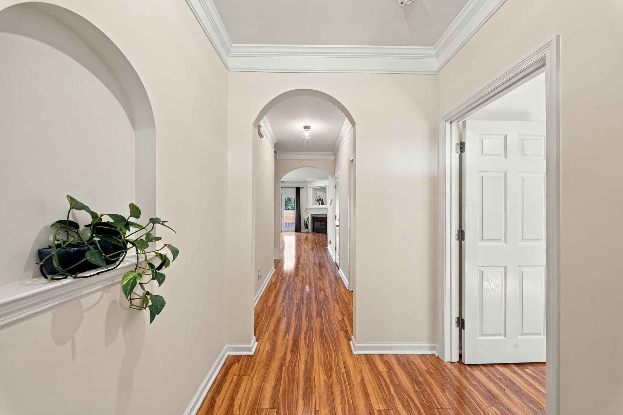 Hallway with hardwood floors, arched openings, a trailing plant, and a fireplace in the distance.