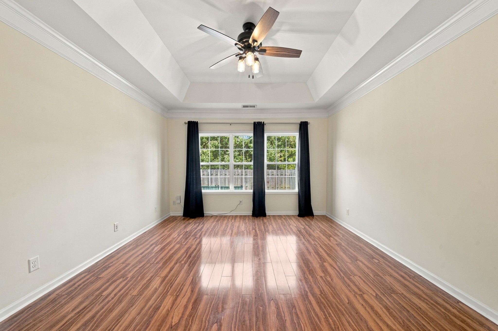 Empty room with polished wood-look floors, a tray ceiling, and two curtained windows.