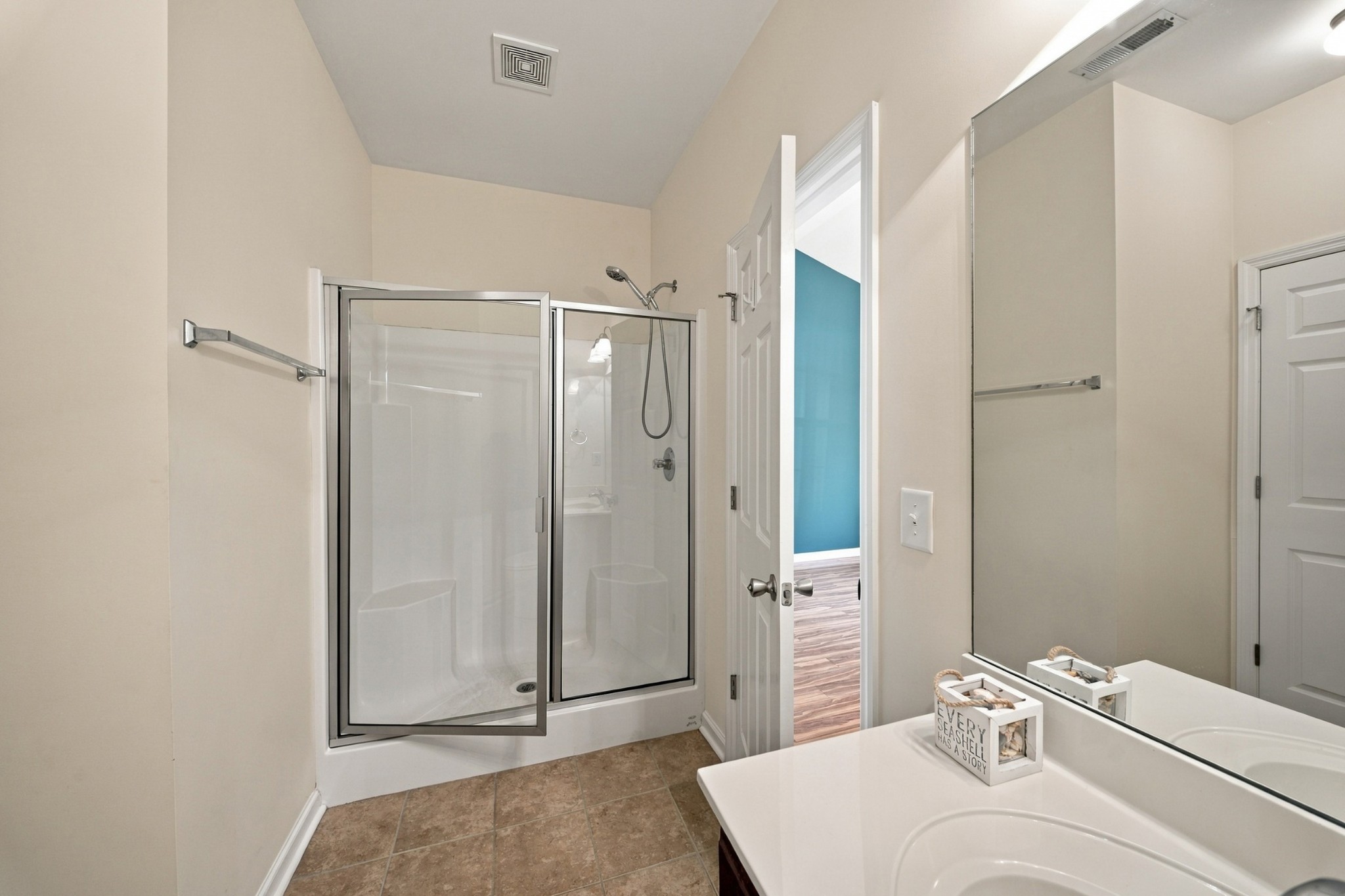 Bathroom with glass-enclosed shower, tiled floor, and white vanity beside an open doorway.