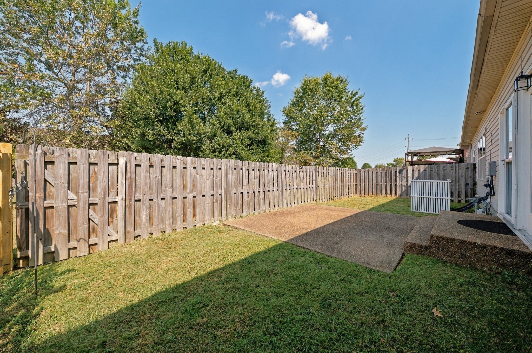 Fenced backyard with a lawn, wooden privacy fence, and paved patio beside the house.