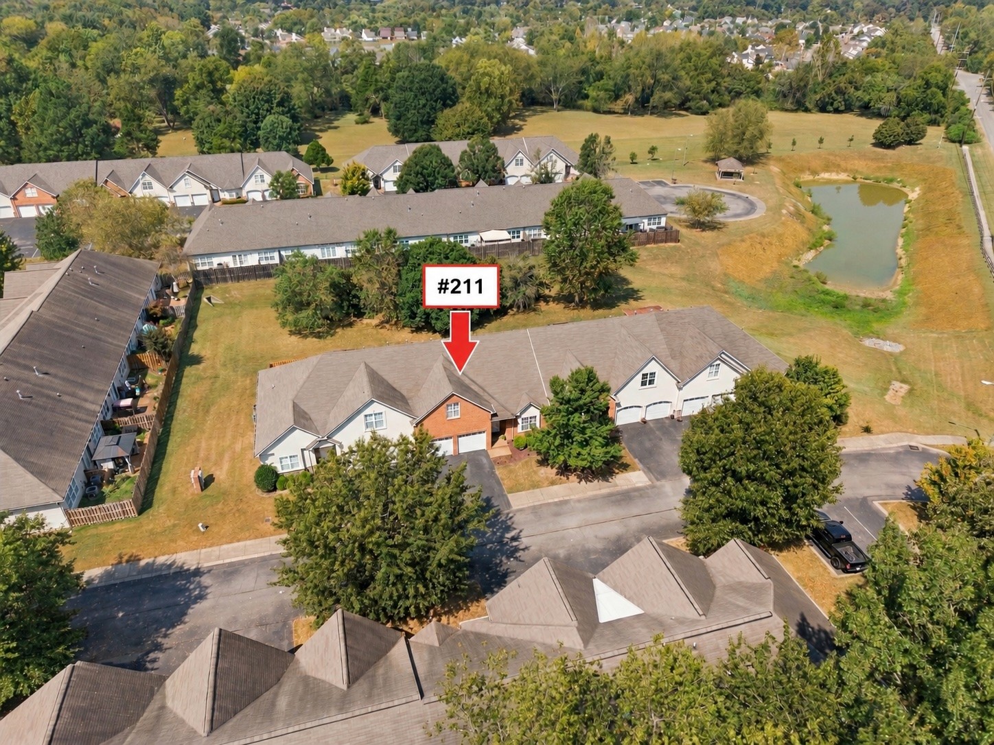 Aerial view of townhouse unit 211, marked by a red arrow beside the community pond.