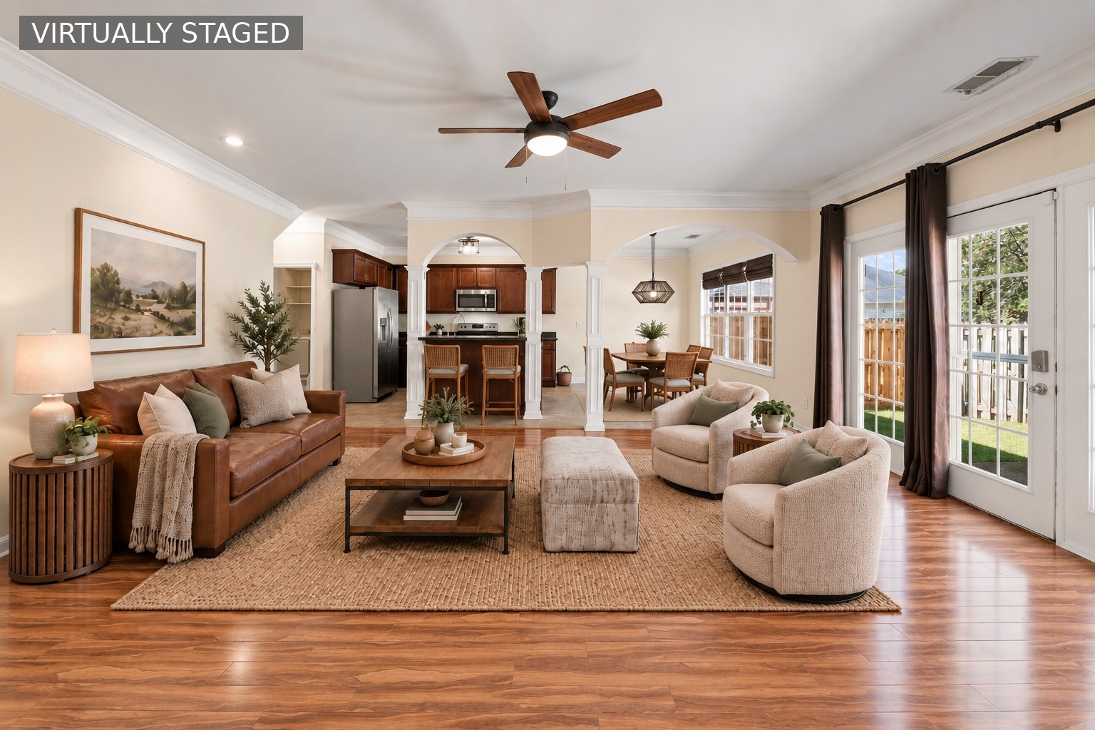Open-plan living room with leather sofa, cream armchairs, wood floors, and adjoining kitchen and dining area.