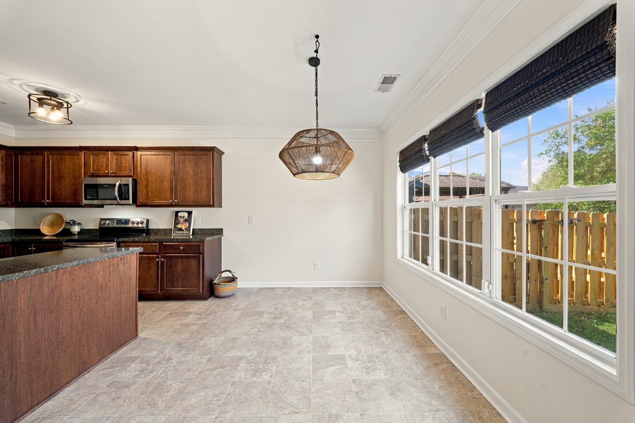 Kitchen with dark wood cabinets and granite counters beside large windows overlooking a fenced yard.