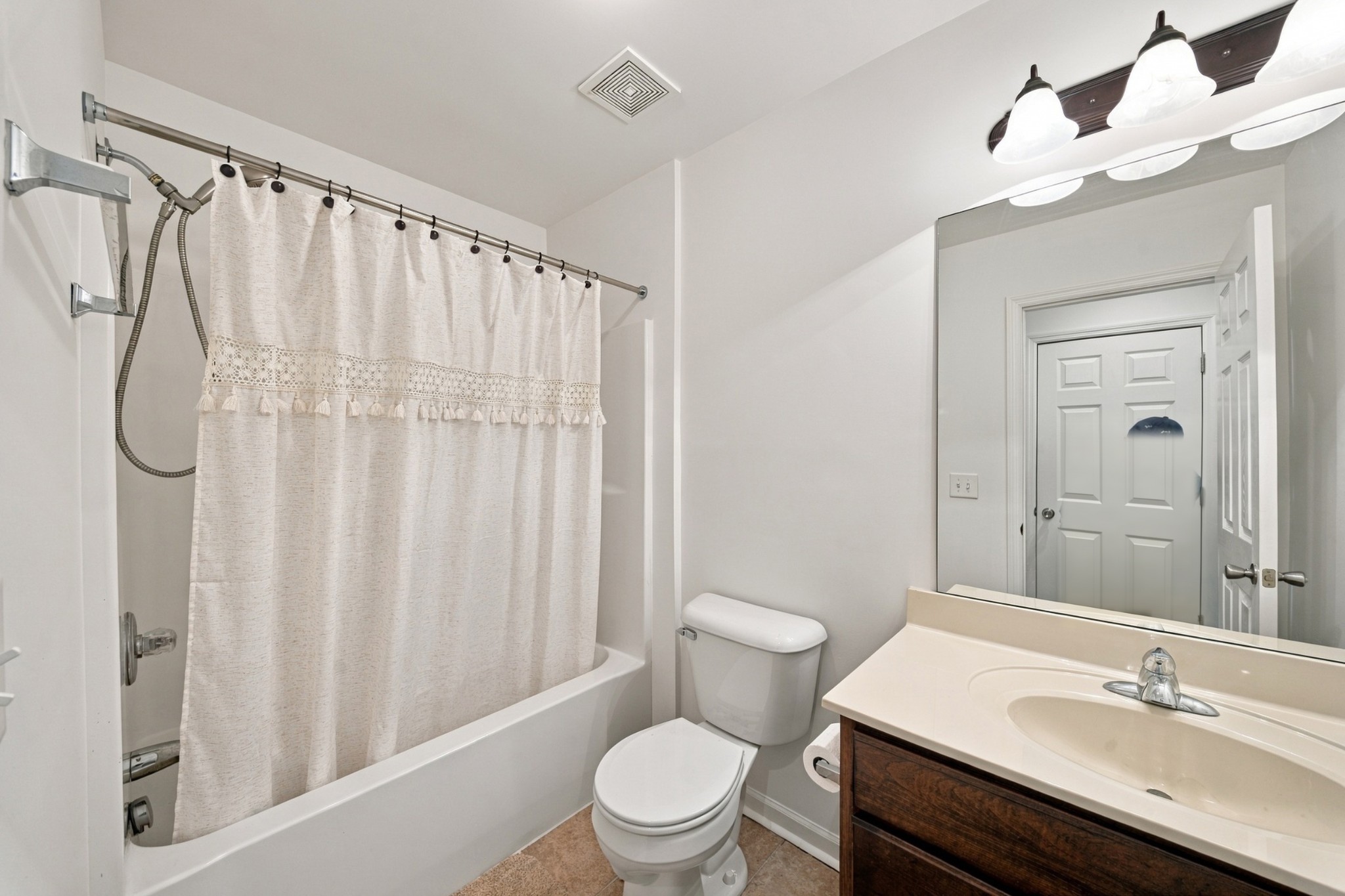 Bathroom with a white-curtained bathtub, toilet, and dark wood vanity.