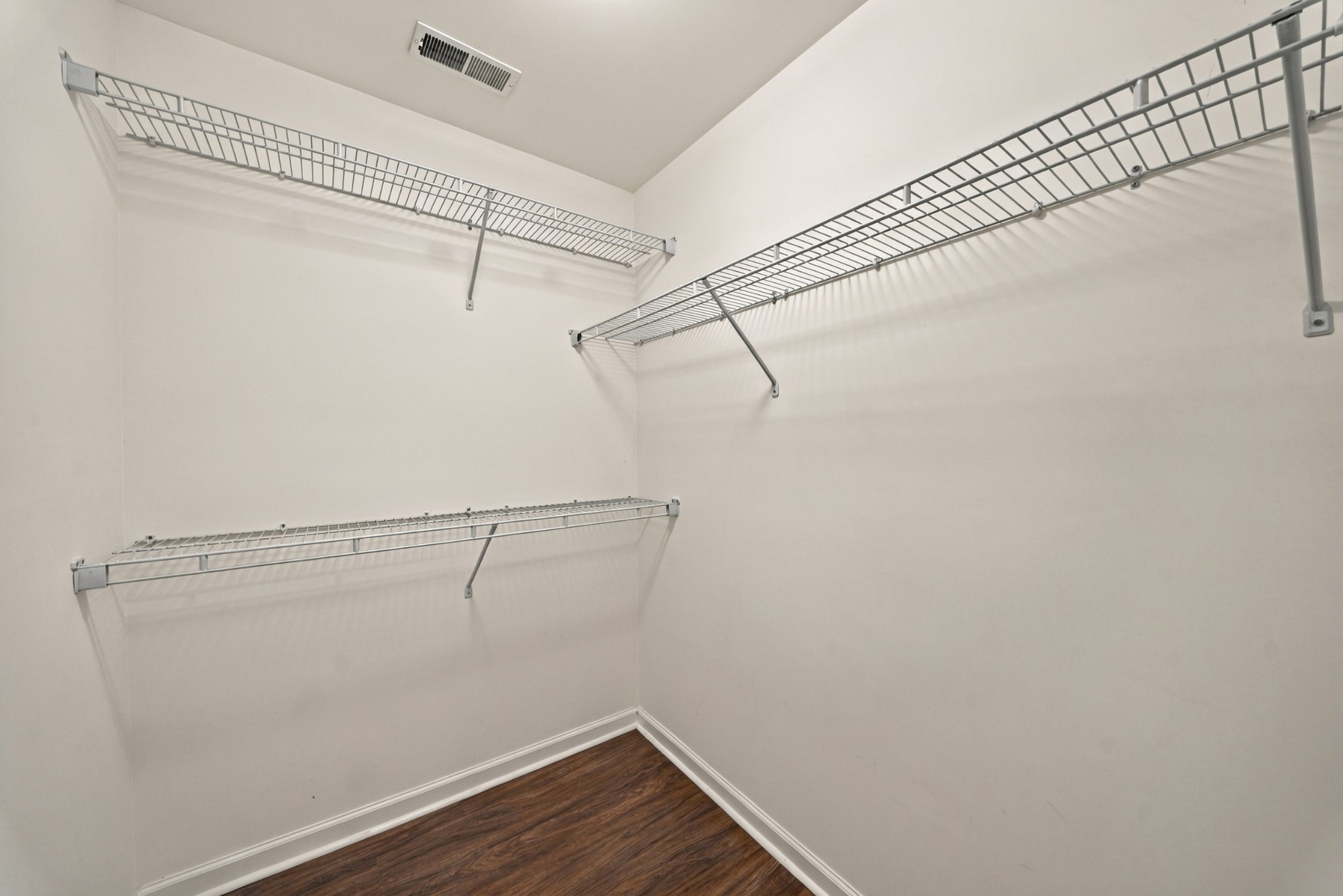 Walk-in closet with wraparound wire shelving and dark wood-look flooring.