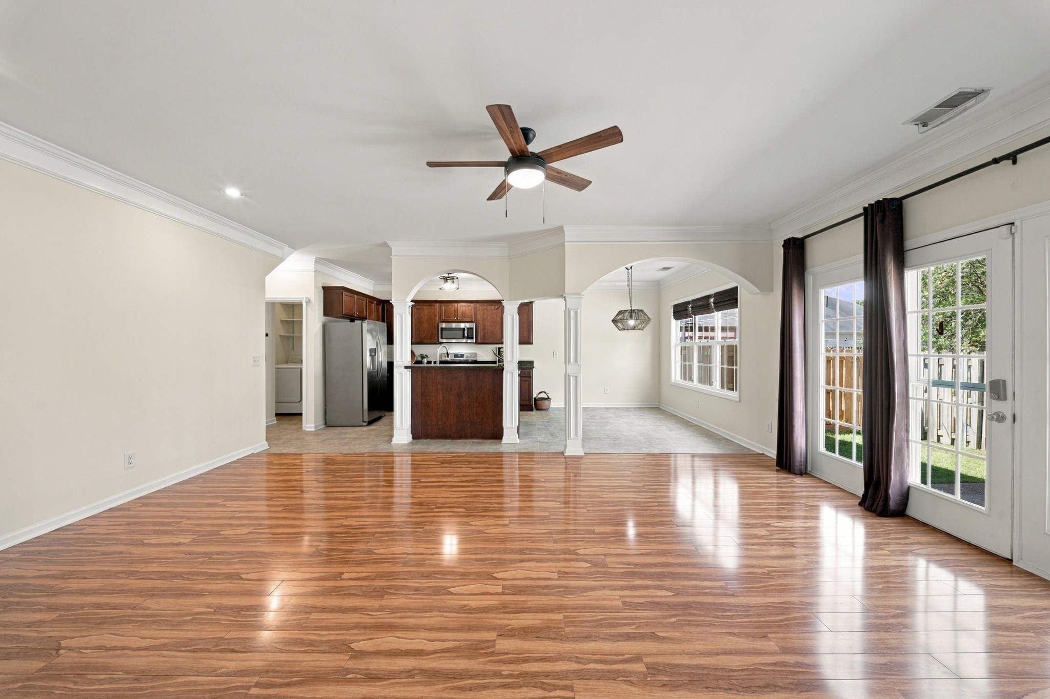 Open-plan living and dining room with glossy wood floors, arched openings, and a kitchen beyond.
