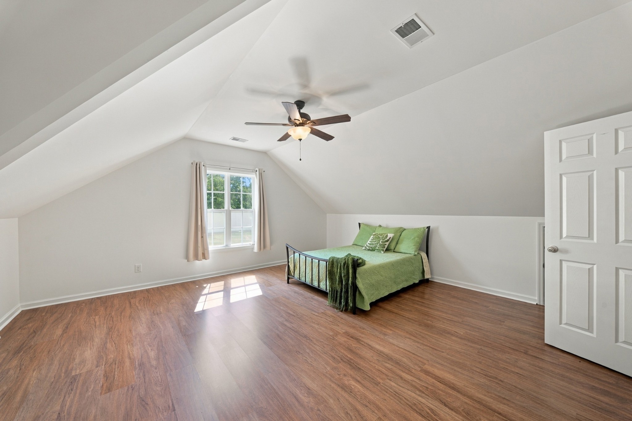 Bedroom with a vaulted ceiling, wood flooring, and a bed dressed in green bedding.