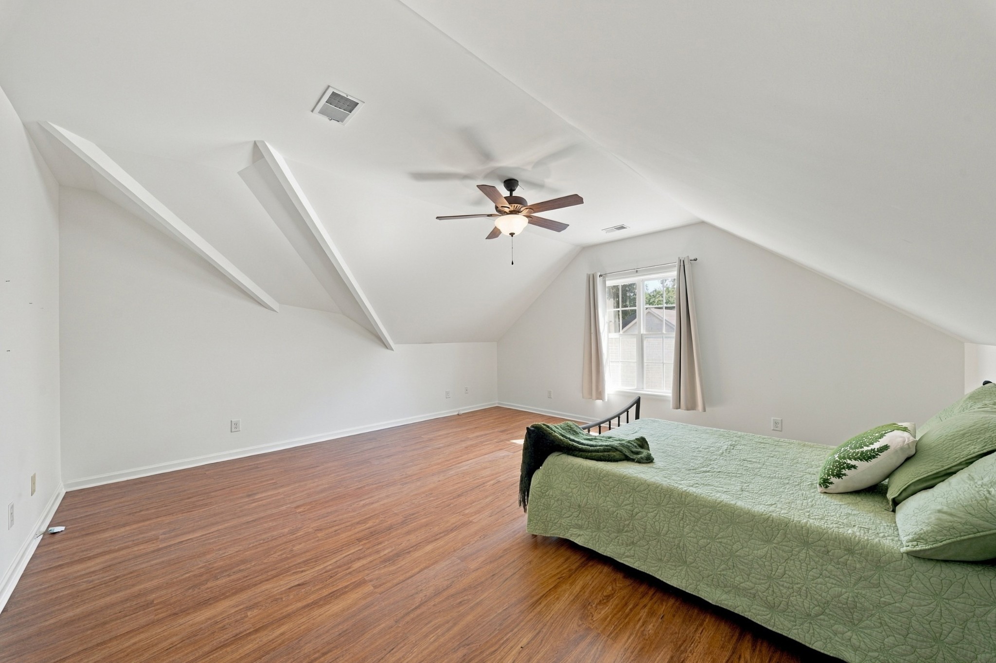 Bedroom with a green quilted bed, wood floors, and a high sloped ceiling with decorative beams.