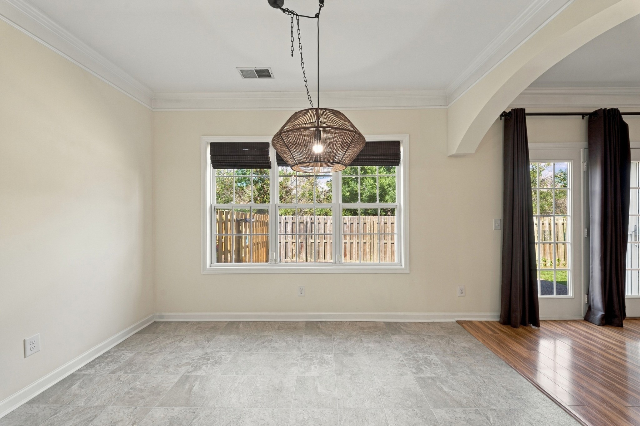 Empty dining area with a woven pendant light, large windows, gray tile, and an adjoining wood floor.