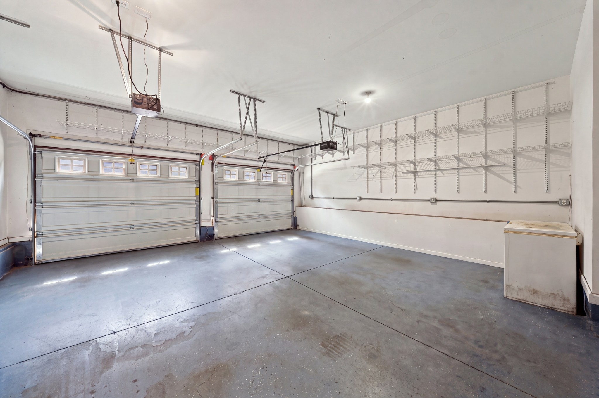 Two-car garage with overhead doors, wall-mounted wire shelves, and a chest freezer.