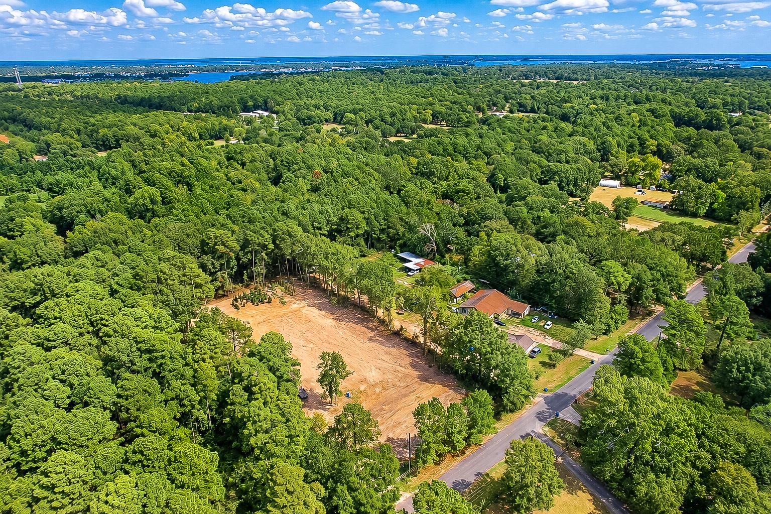 Aerial view of wooded property with a large cleared area beside a paved road.