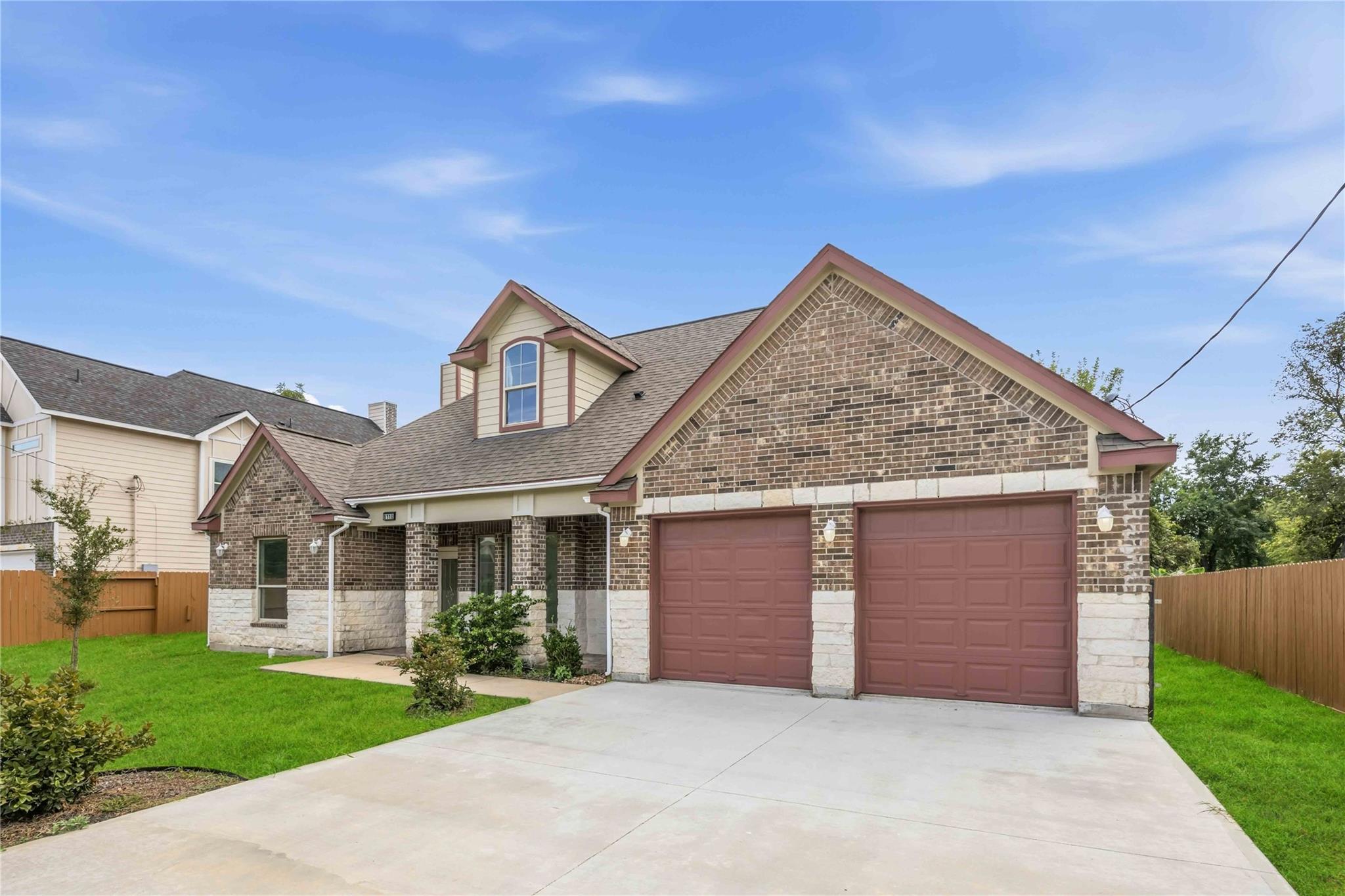 Two-story brick-and-stone house with two red garage doors and a broad concrete driveway.