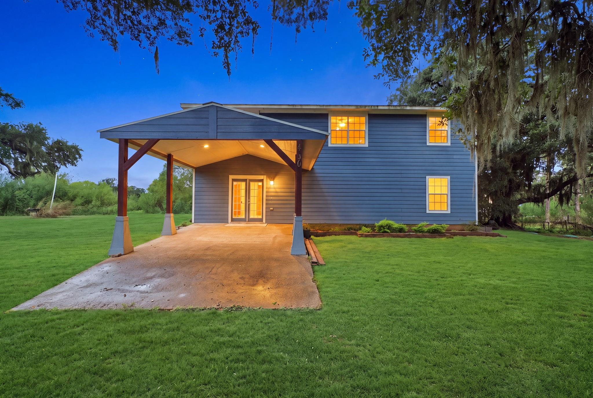 Blue-sided two-story home with a broad covered carport and warmly lit windows at dusk.