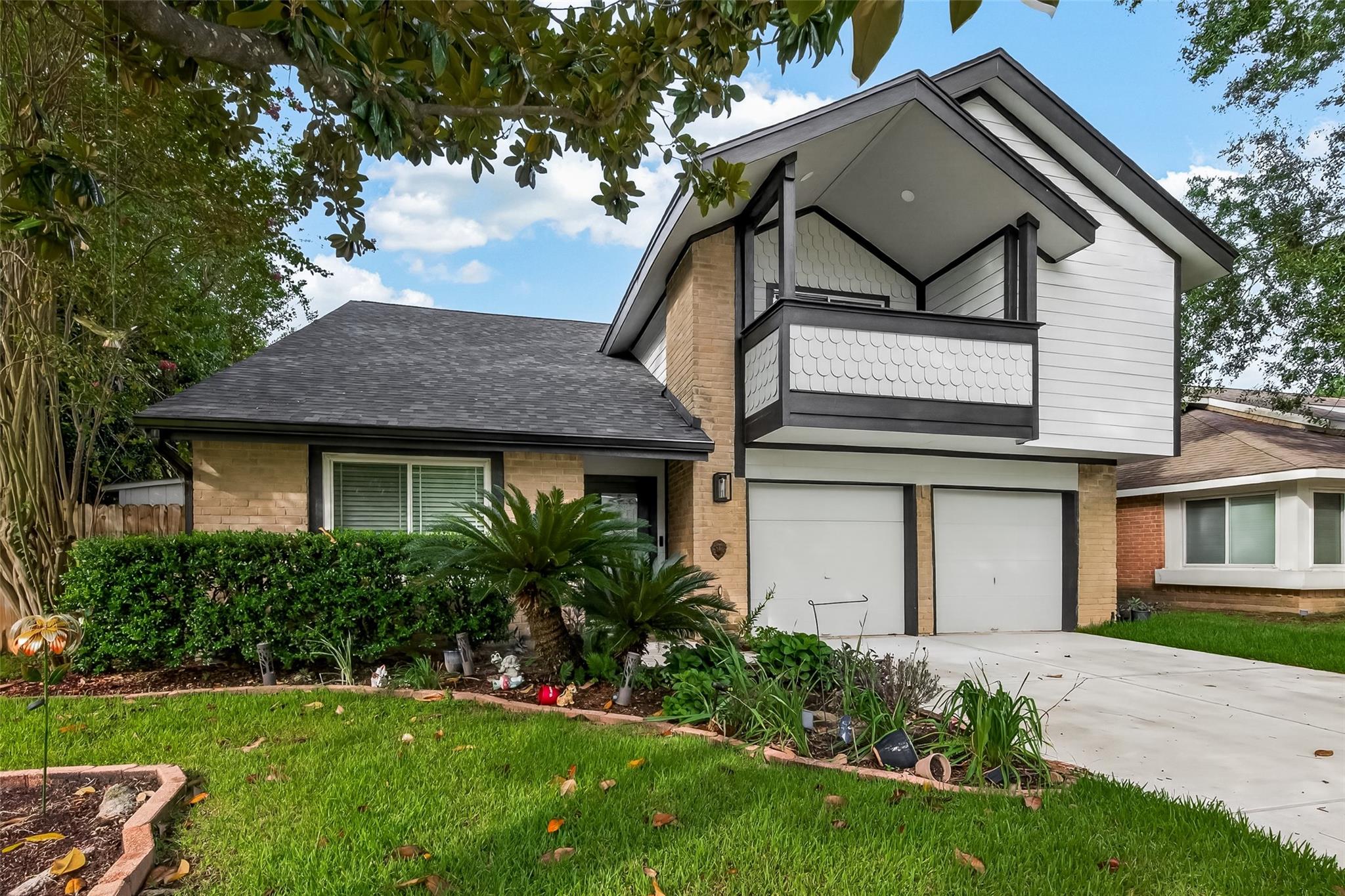 Two-story brick and white-sided house with an upper balcony, double garage, and landscaped front lawn.