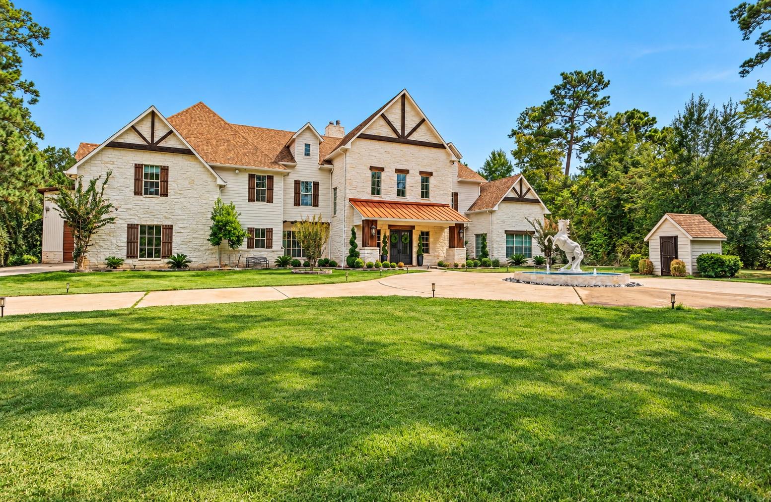 Large stone house with copper entry awning, manicured lawn, horse fountain, and detached outbuilding.