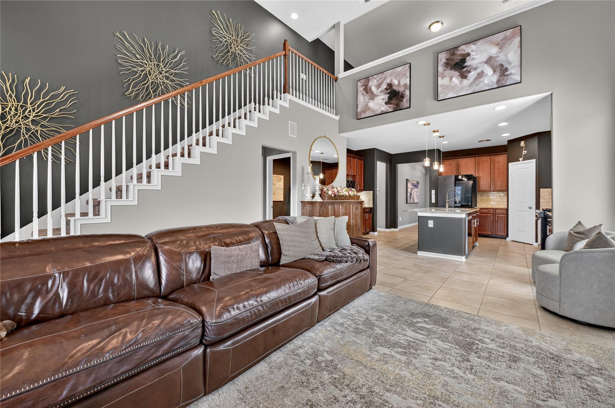 Open-plan living room with a brown leather sectional, staircase, and kitchen island.
