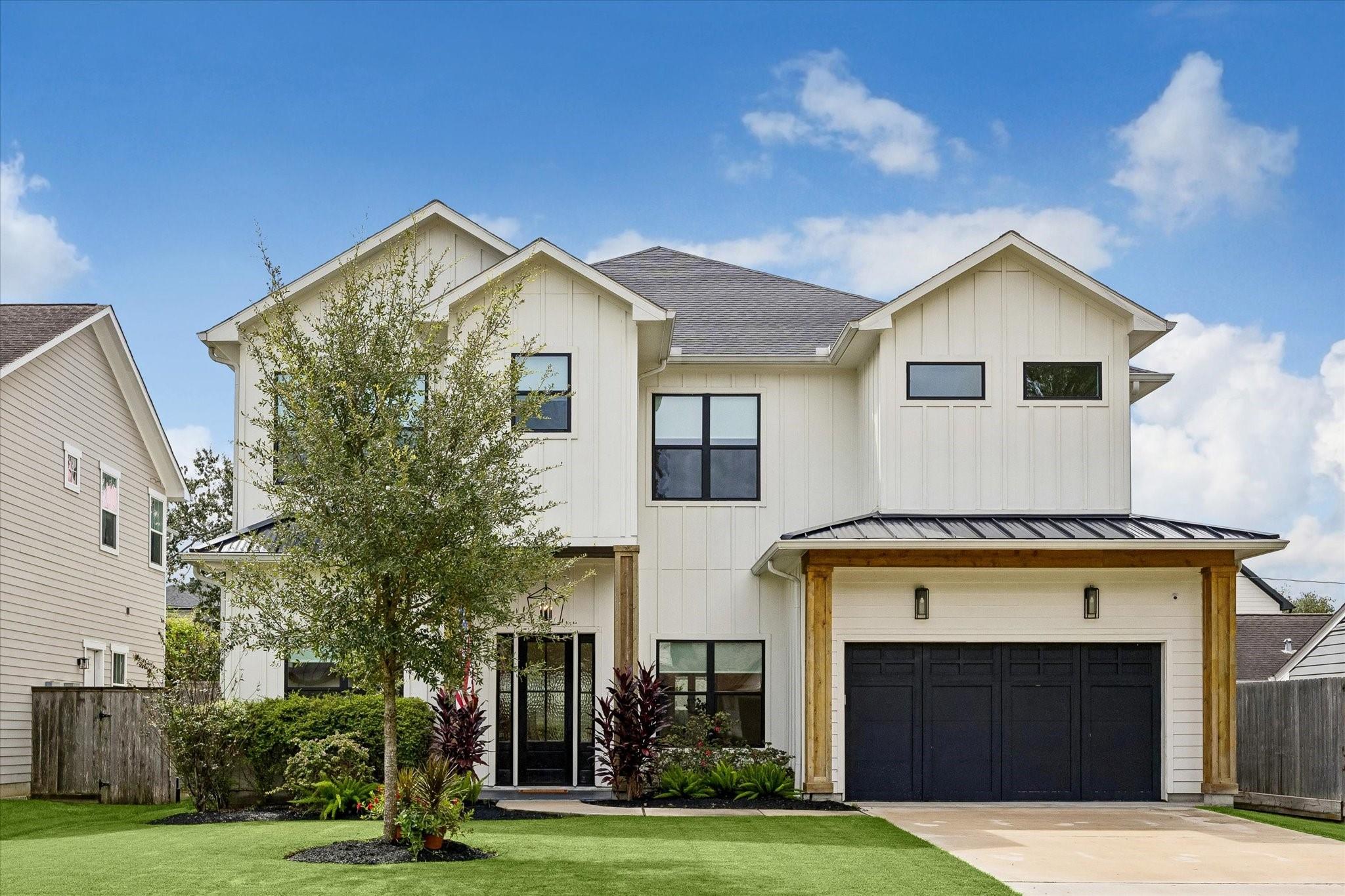 Two-story white house with black-framed windows, a dark double garage, and landscaped front lawn.