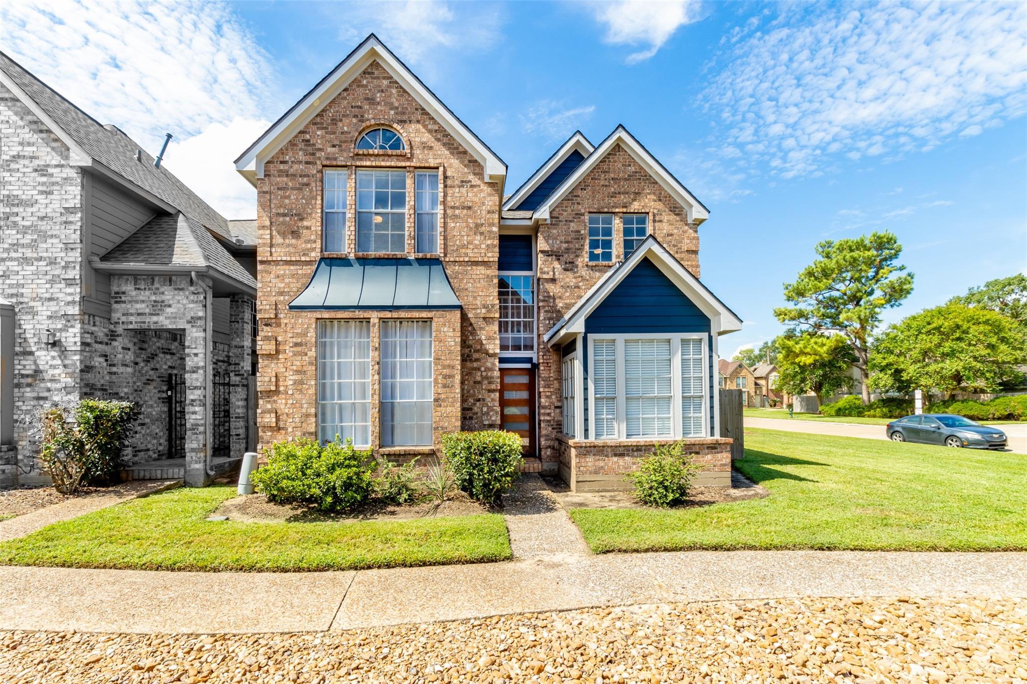 Two-story brick house with blue gables, large windows, and a landscaped front lawn.