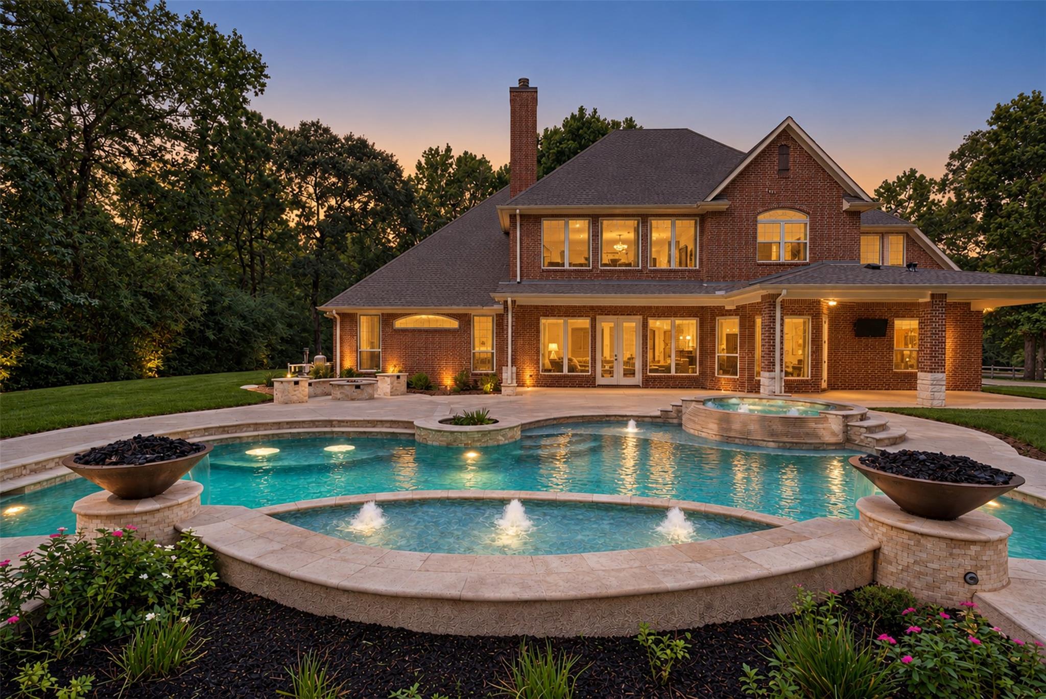 Two-story brick house behind an illuminated pool with fountains and a raised spa at dusk.