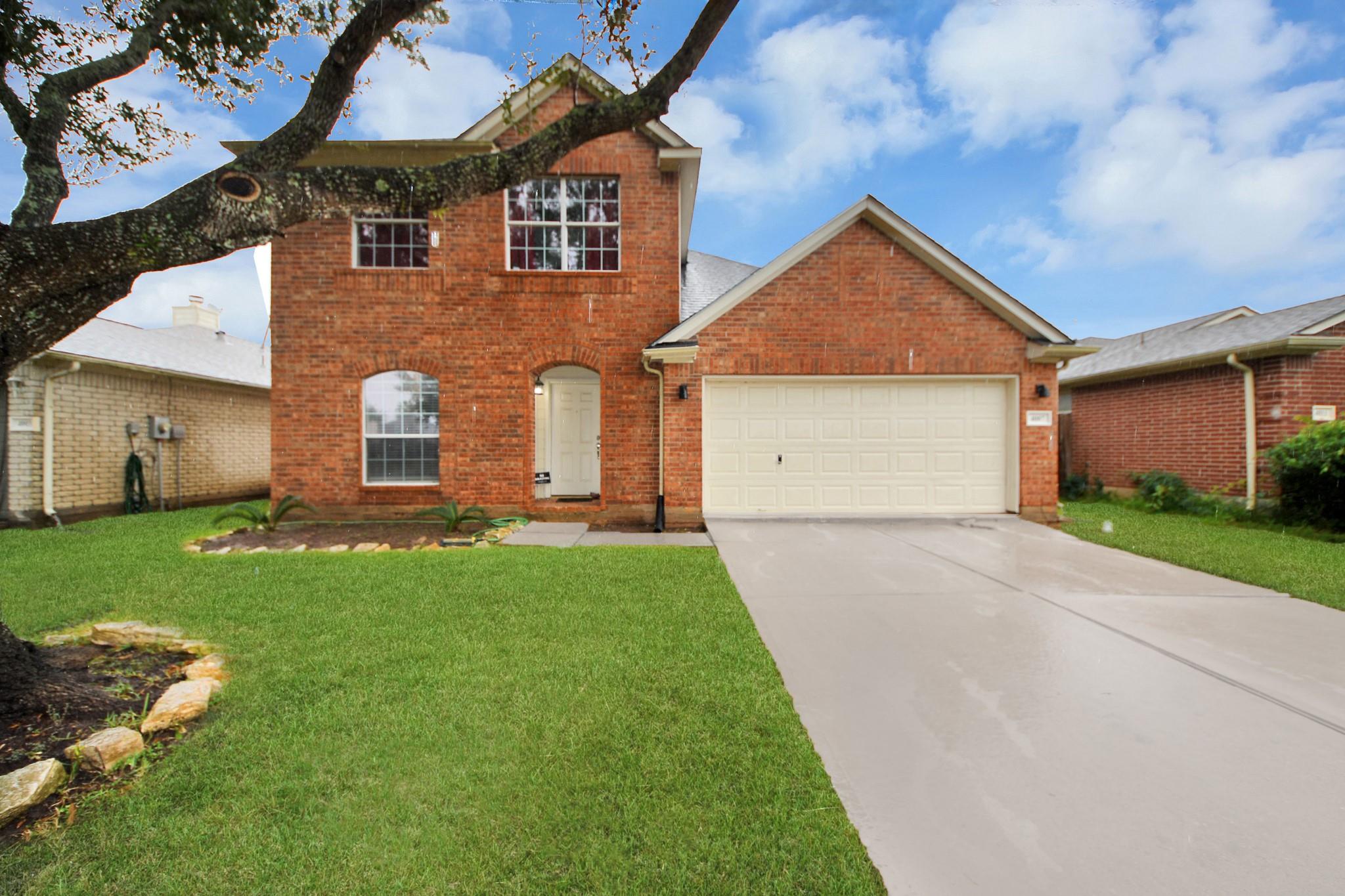 Two-story red-brick house with an attached double garage, broad driveway, and a large tree in the front yard.