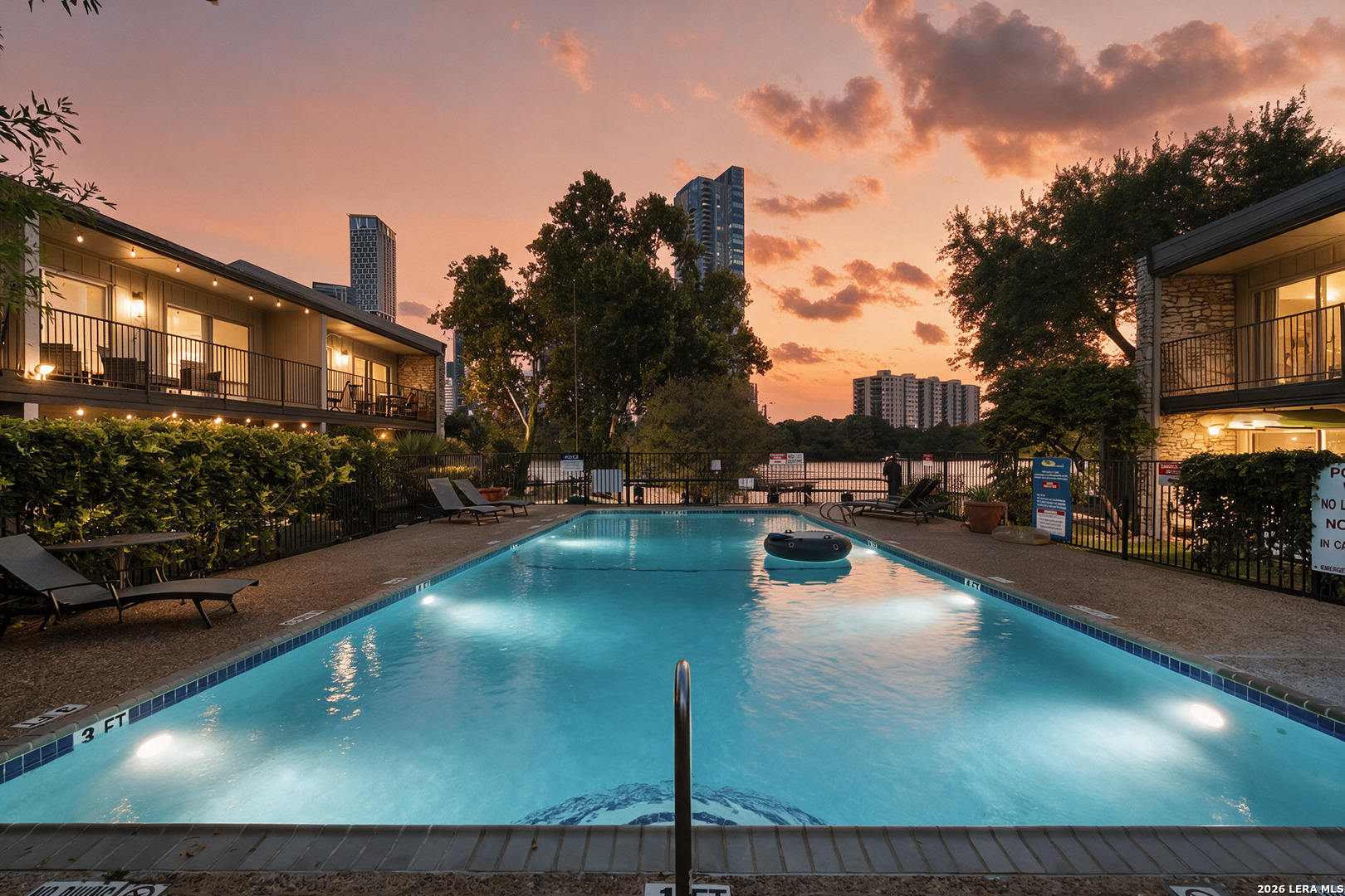 Residential complex pool at dusk, framed by lit balconies and city buildings.