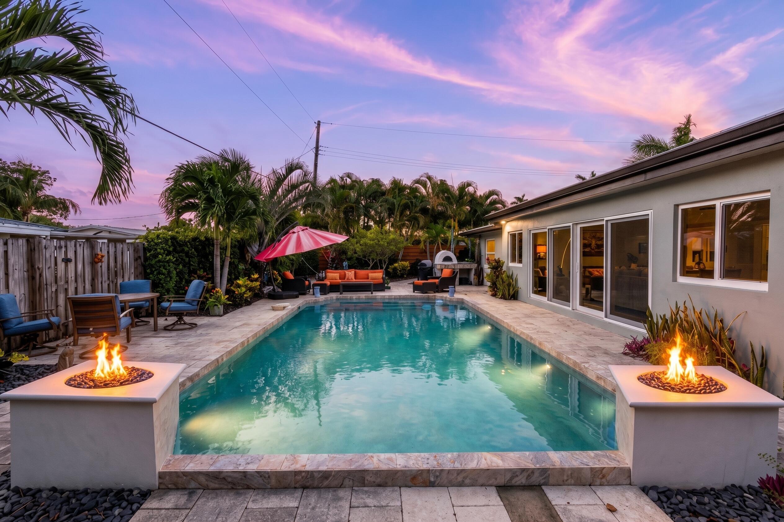 Backyard pool at dusk with twin fire bowls, palm trees, and furnished patio seating.