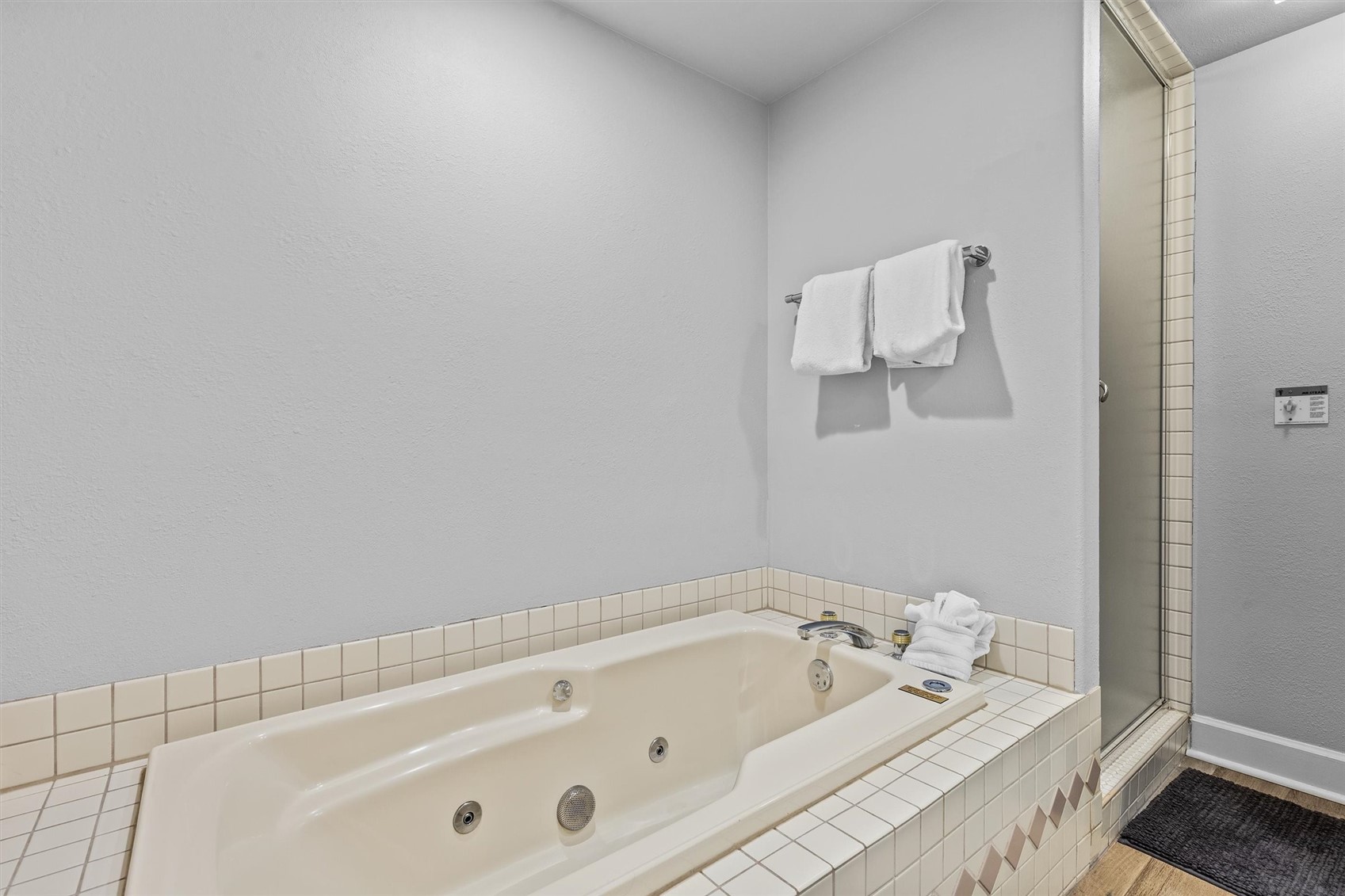Bathroom with a tiled jetted tub, glass shower, and white towels.