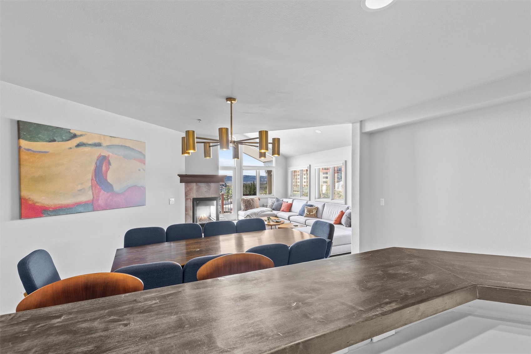 Open dining and living area with a wood table, fireplace, sectional sofa, and mountain views.