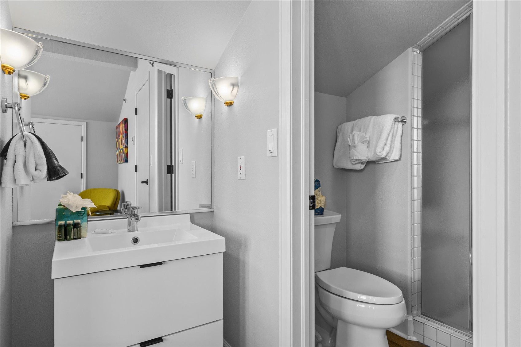Bathroom with a white vanity, large mirror, toilet, and glass-enclosed shower.