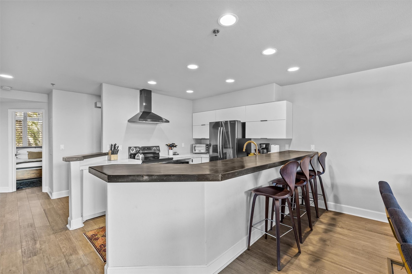 Modern kitchen with white cabinets, stainless steel appliances, and a long island lined with bar stools.